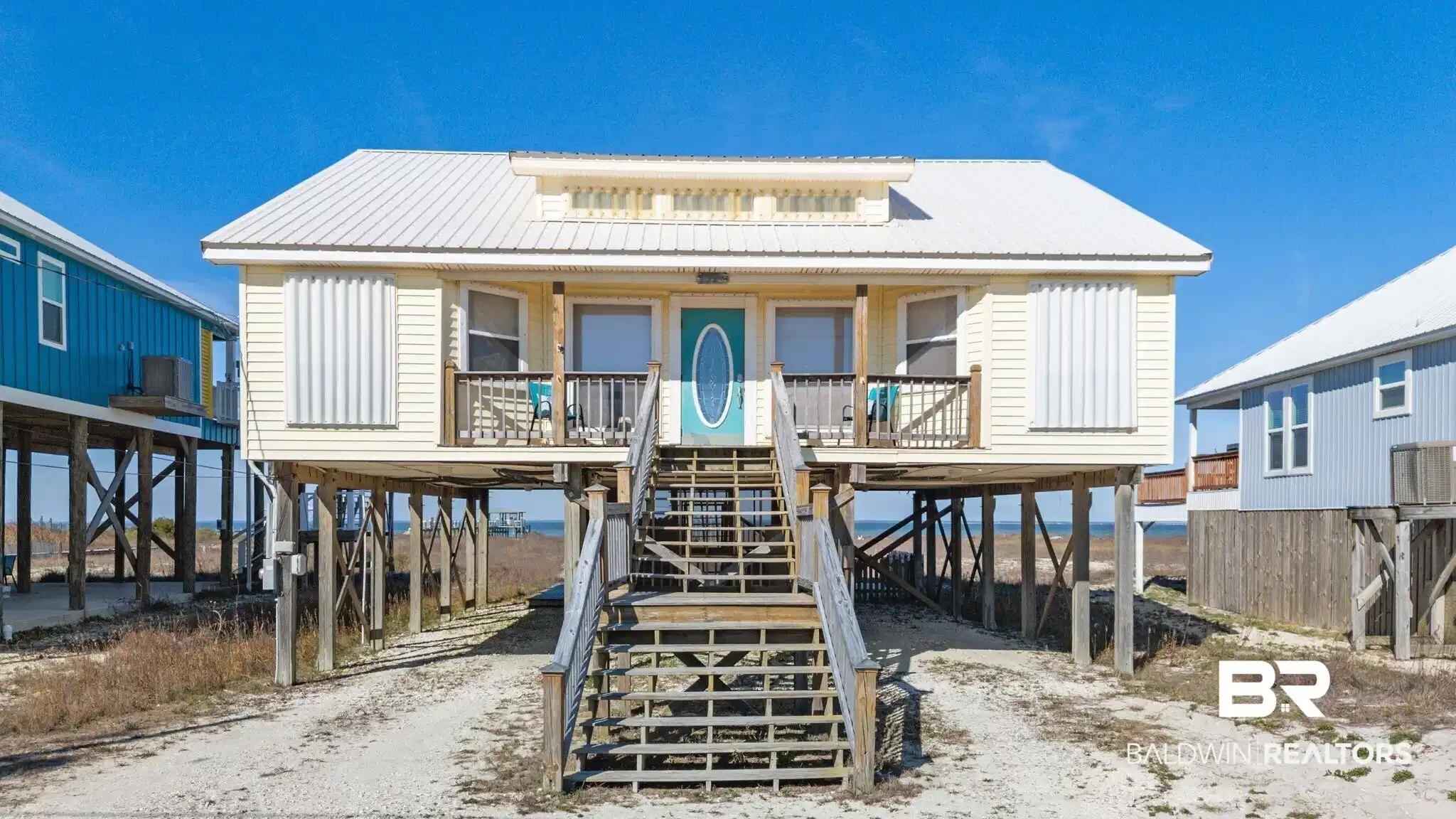 Image 1: Raised beach house with a carport, a metal roof, driveway, and stairway