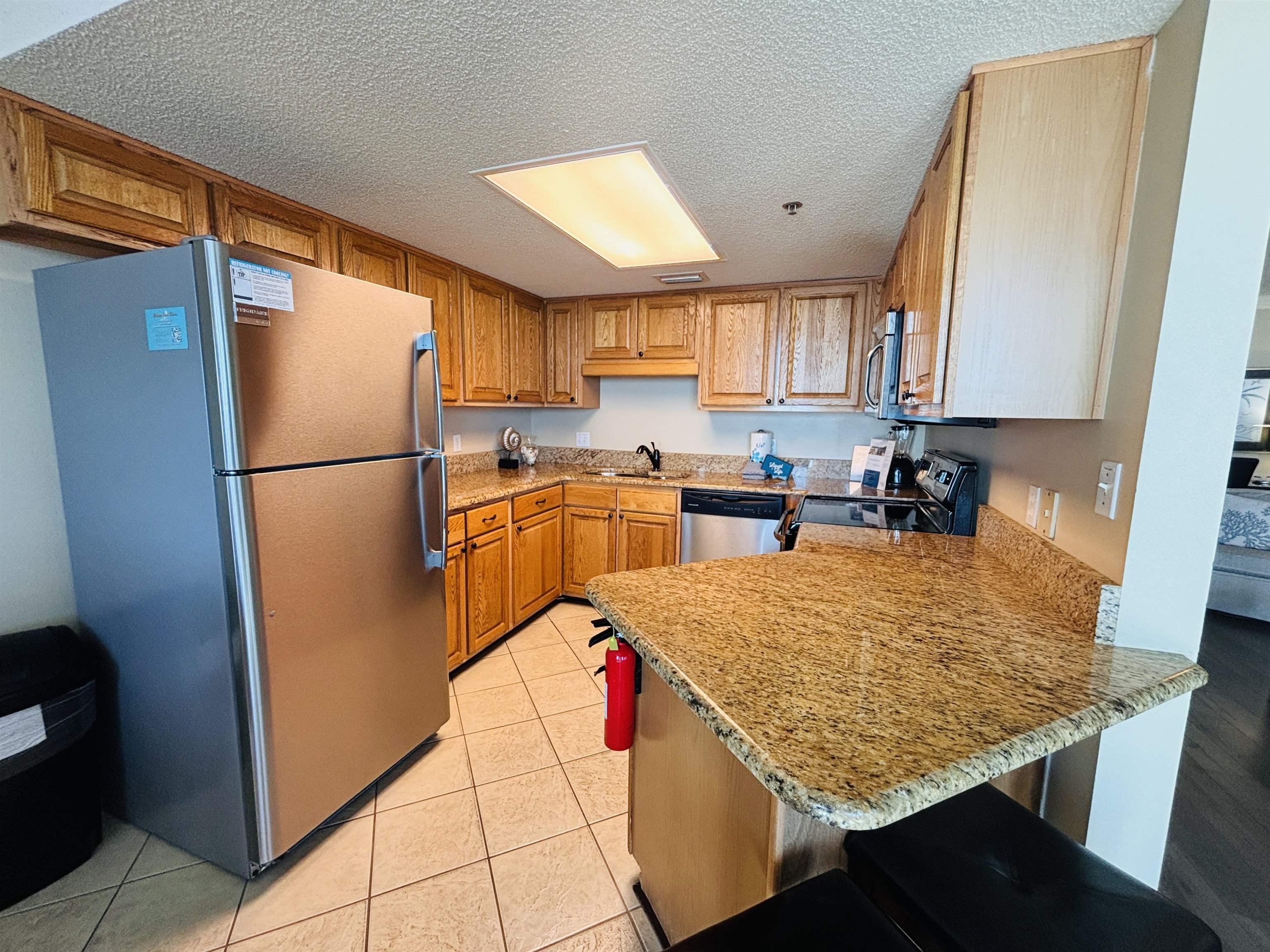 Image 3: Kitchen featuring stainless steel appliances, a textured ceiling, a peninsula, brown cabinetry, and a breakfast bar area