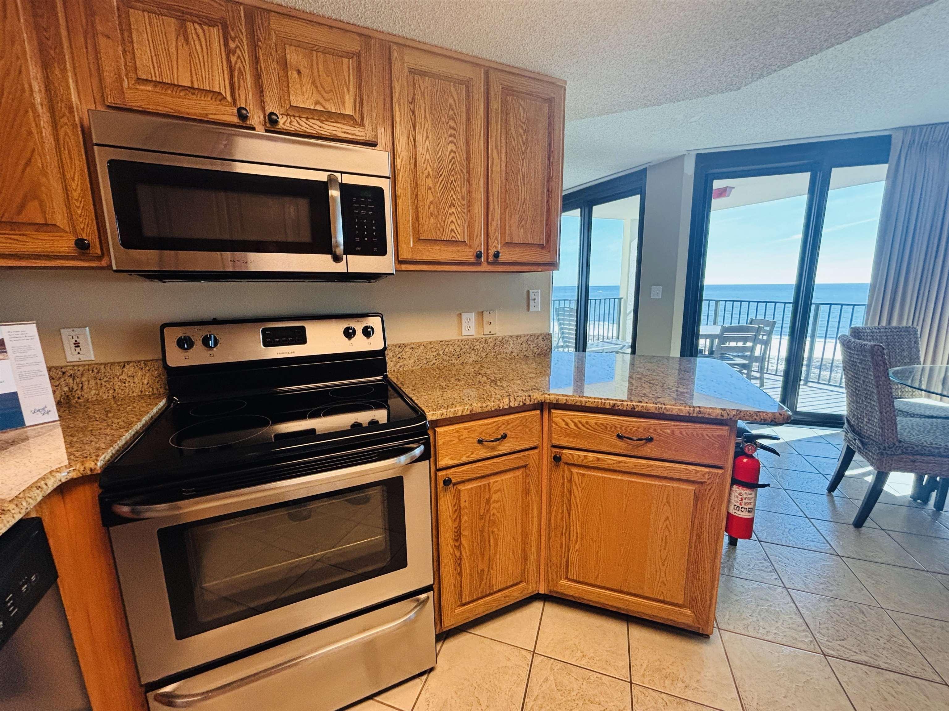 Image 4: Kitchen featuring stainless steel appliances, a textured ceiling, brown cabinets, light stone countertops, and light tile patterned flooring