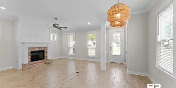 Image 2: Spacious living area featuring light wood-finish flooring, a brick fireplace with a shiplap accent wall, and a ceiling fan