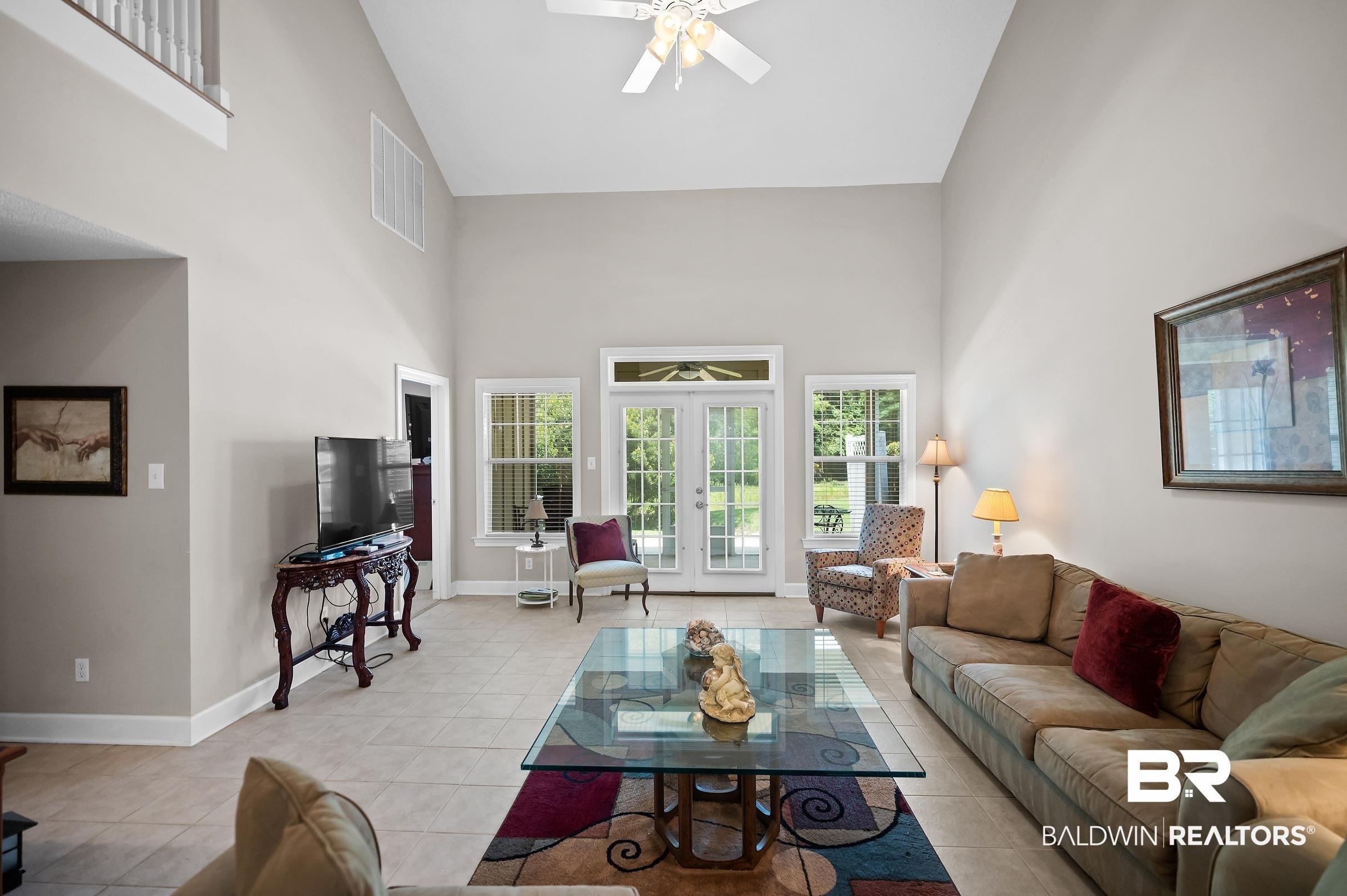 Image 3: Spacious living area featuring vaulted ceilings, light-toned tile flooring, and multiple windows with exterior access