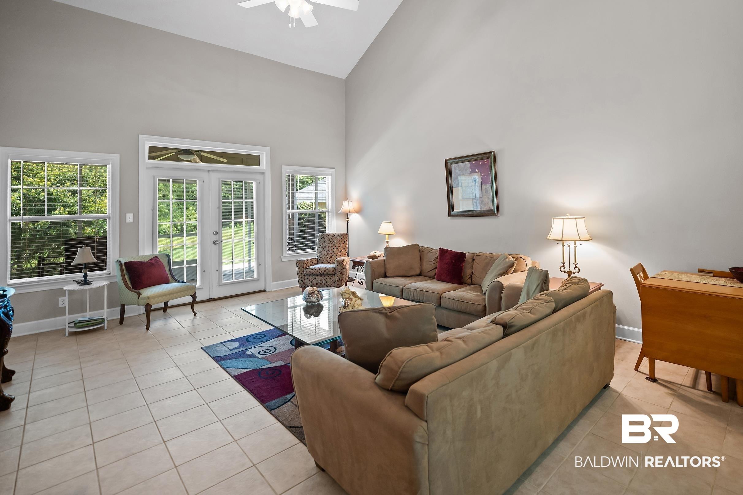 Image 4: Expansive living area featuring a vaulted ceiling with a ceiling fan, light gray painted walls, and tile flooring