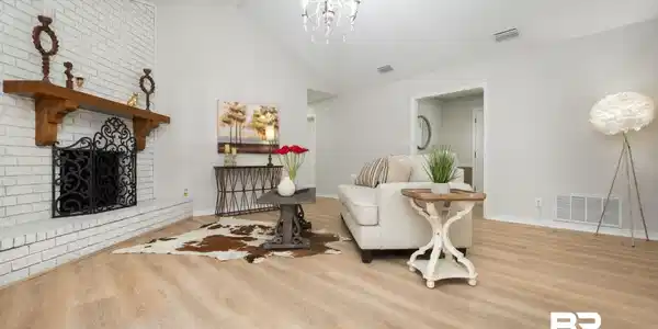 Image 2: Spacious living area featuring a vaulted ceiling with chandelier, light wood-finish flooring, and a white brick fireplace with a wood mantel