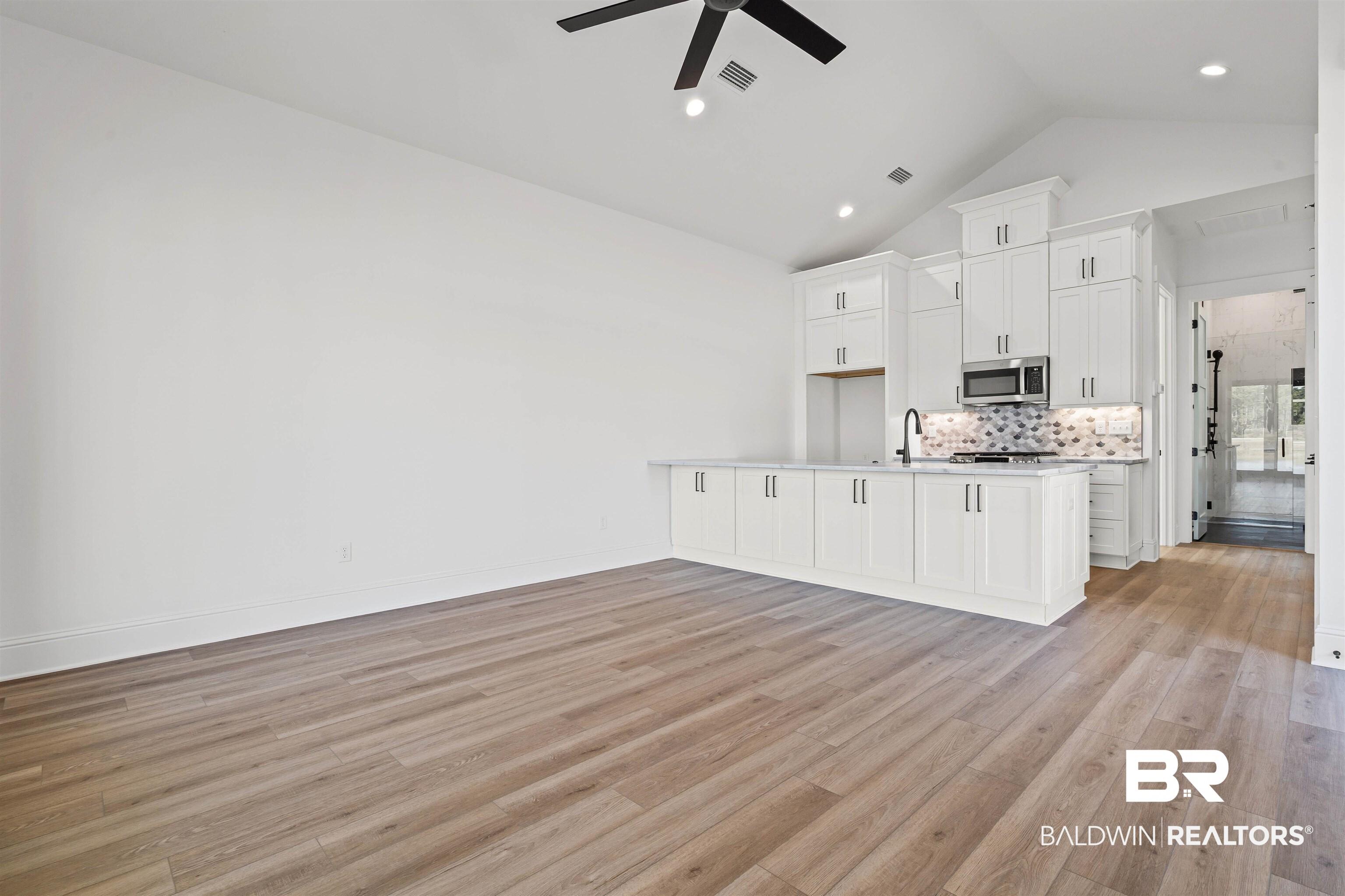 Image 3: Kitchen featuring white cabinetry, open floor plan, light wood-style flooring, tasteful backsplash, and high vaulted ceiling