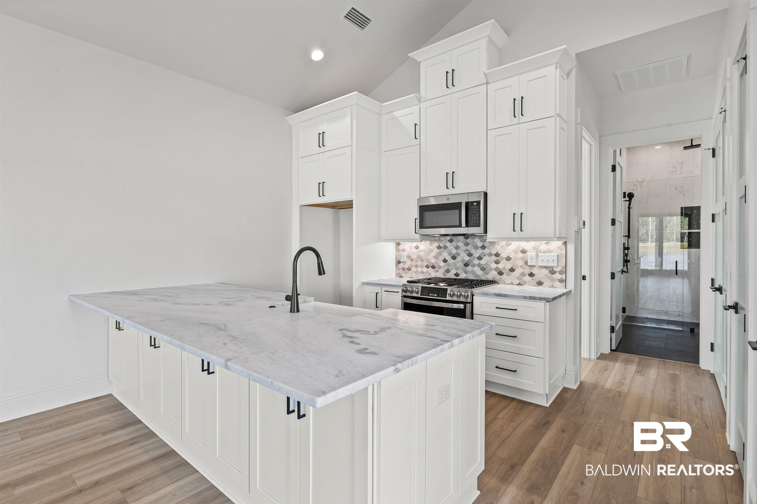 Image 4: Kitchen with white cabinetry, stainless steel appliances, light stone counters, backsplash, and light wood-style floors