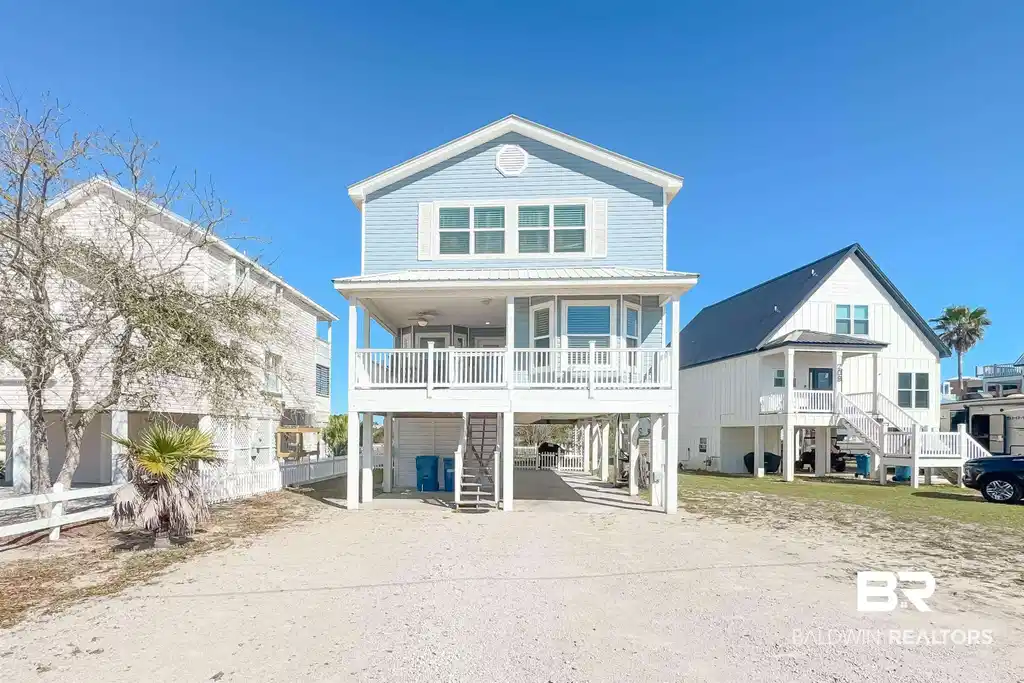 Image 1: Coastal inspired home with a carport, a wooden deck, dirt driveway, a patio, and a metal roof