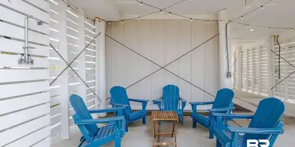 Image 4: Covered outdoor patio featuring a privacy-screened outdoor shower with chrome fixtures, string lighting, and exposed ceiling beams
