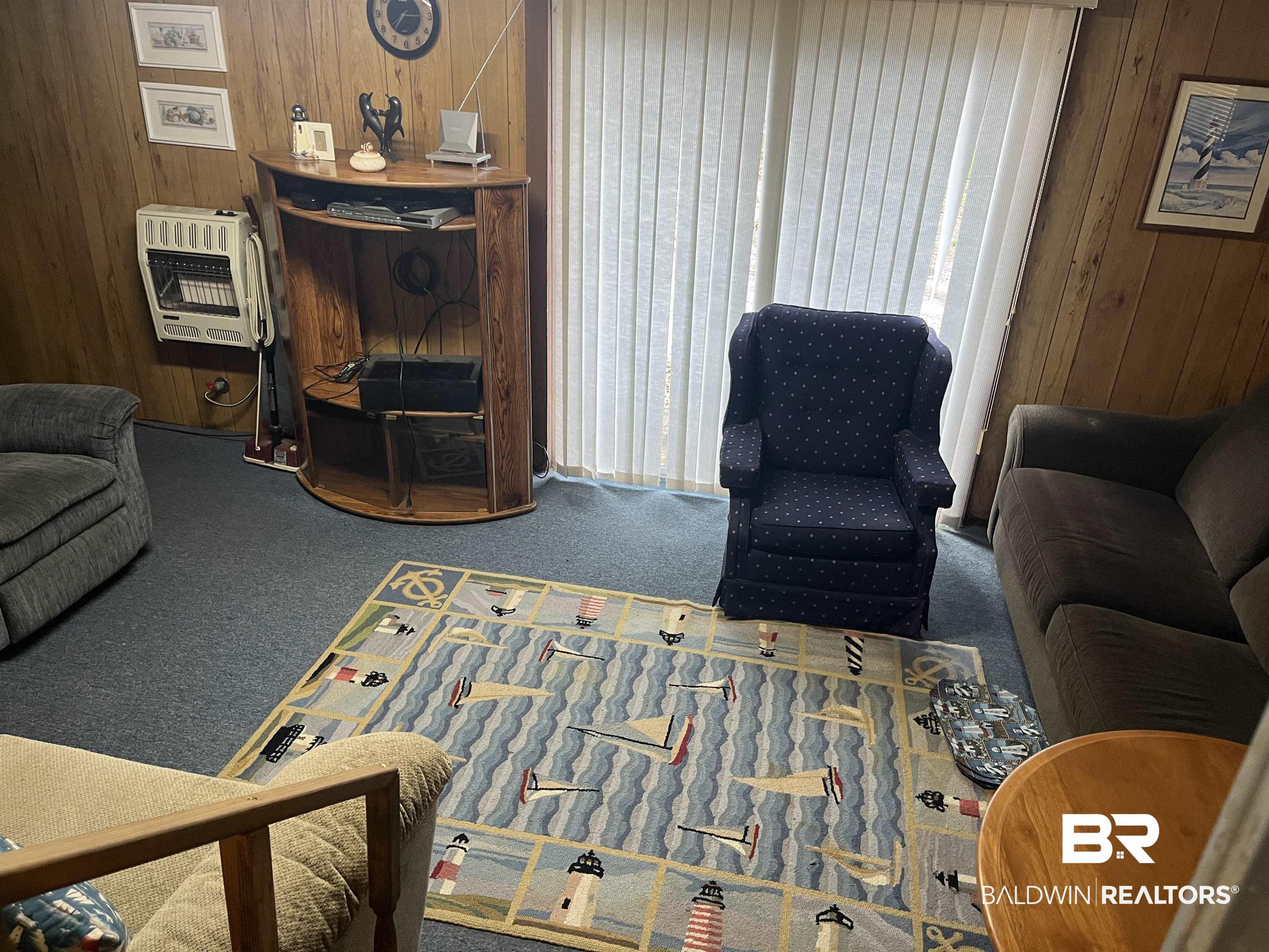 Image 4: Wood paneling walls featuring a wall-mounted heater, blue carpet flooring, and vertical blinds on the window