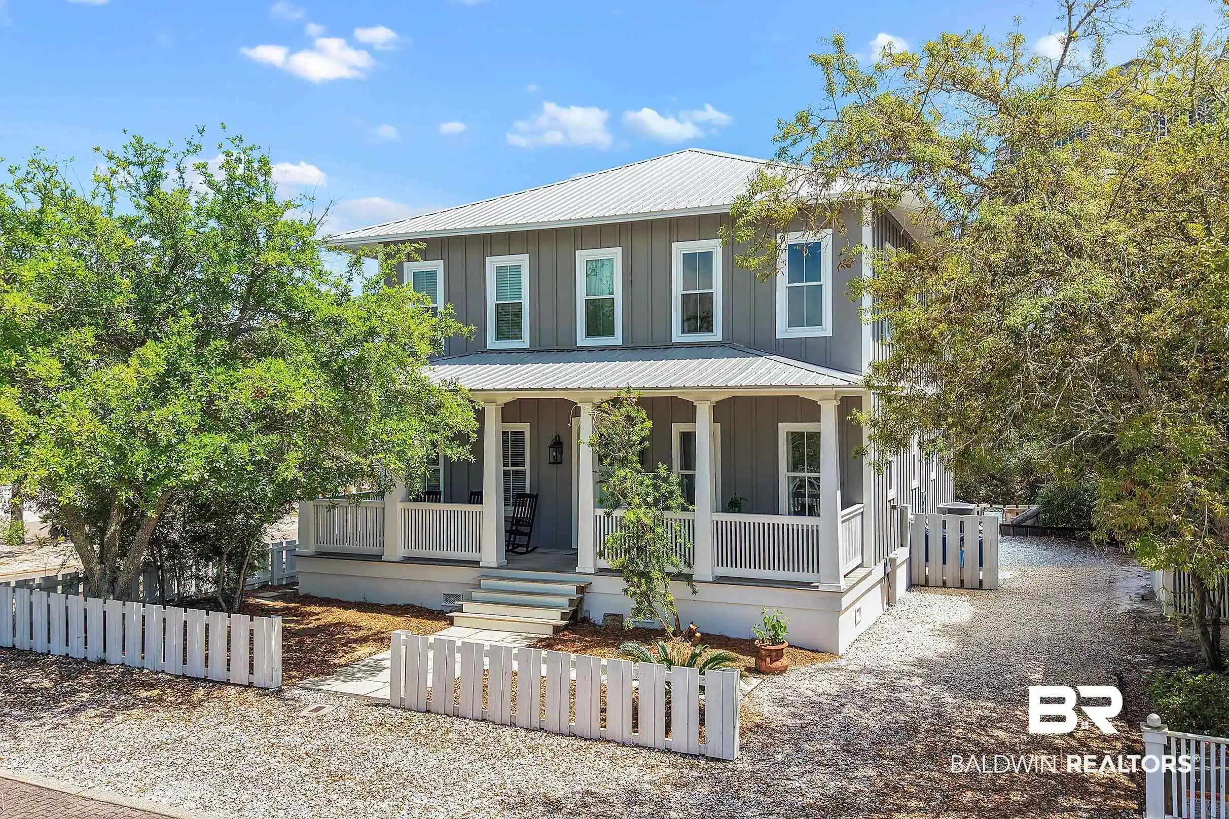 Image 1: Two-story residence featuring board and batten siding, a metal roof, and a covered front porch with white railings and columns