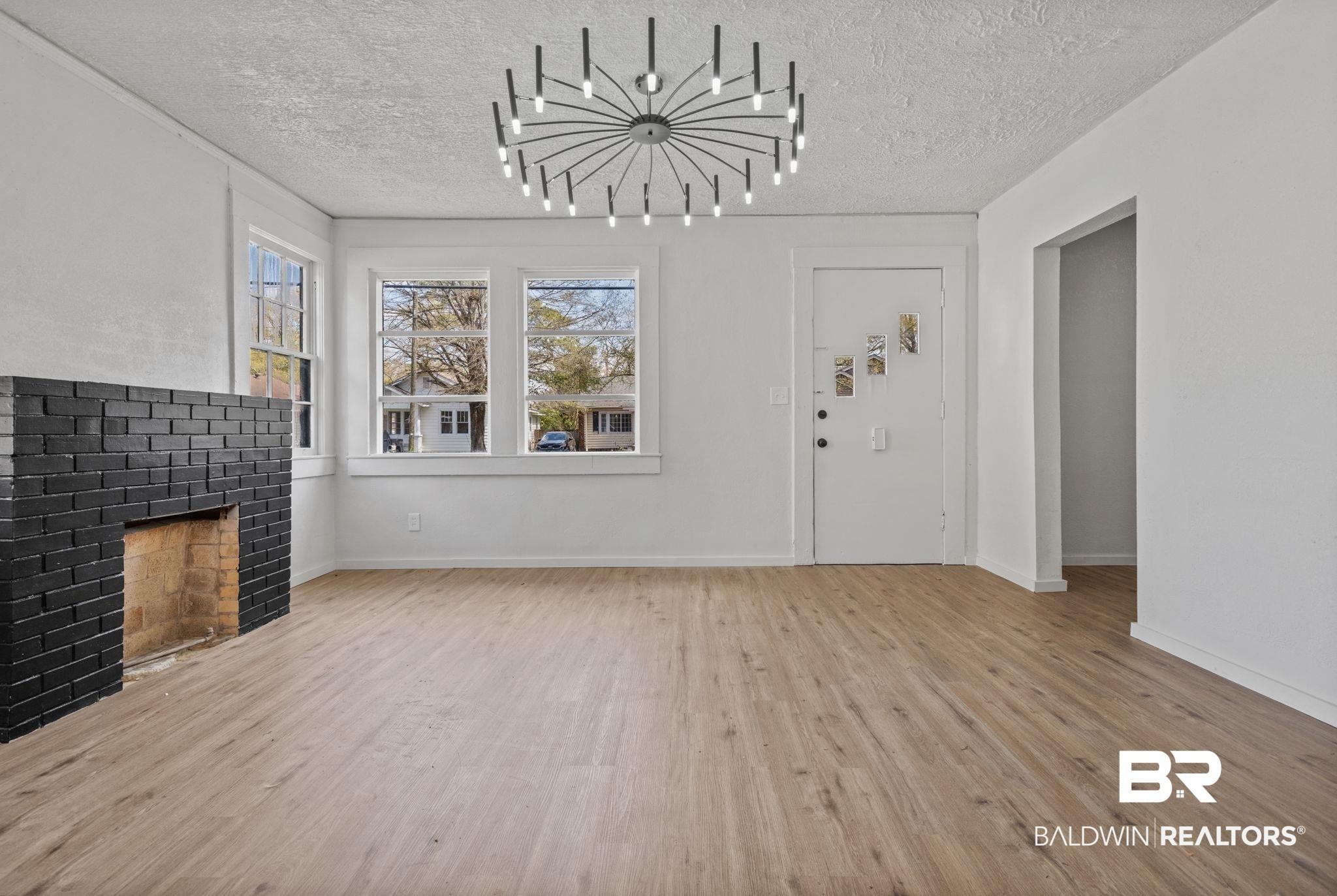 Image 3: Unfurnished living room with light wood-style floors, a brick fireplace, suspended lighting, and a textured ceiling