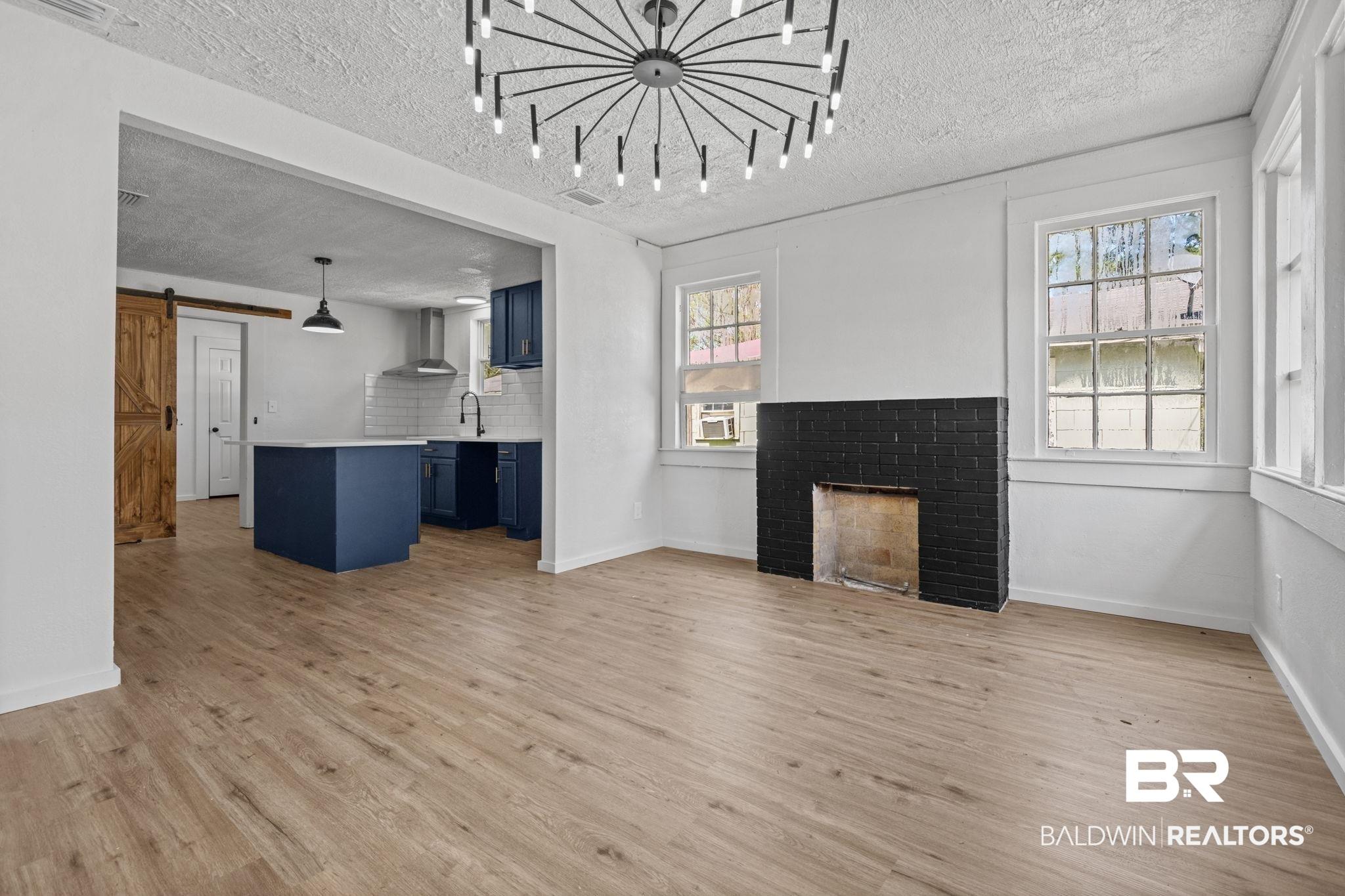 Image 4: Unfurnished living room with a barn door, a brick fireplace, light wood-style floors, and a textured ceiling