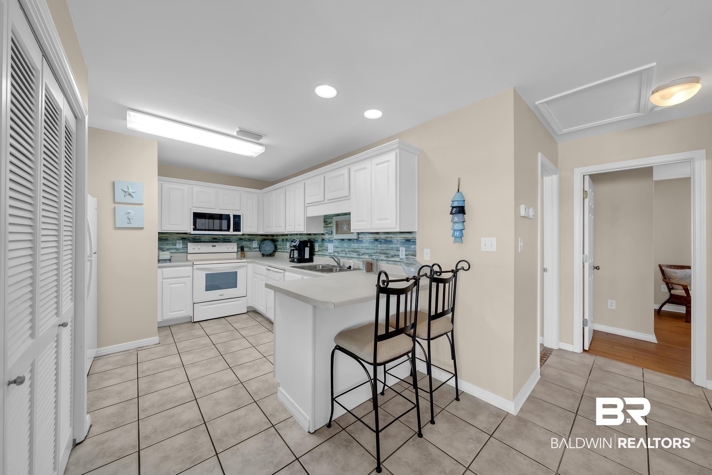 Image 4: Kitchen featuring white cabinetry, tile backsplash, built-in microwave, and a breakfast bar with solid surface countertops
