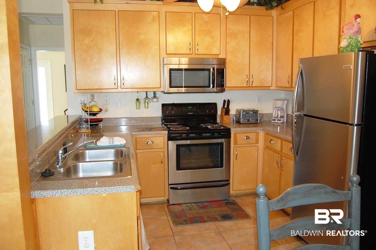 Image 3: Kitchen featuring light wood cabinetry, dark finish countertops, stainless steel appliances, and a double basin sink.