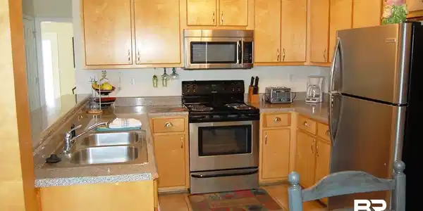 Image 3: Kitchen featuring light wood cabinetry, dark finish countertops, stainless steel appliances, and a double basin sink.