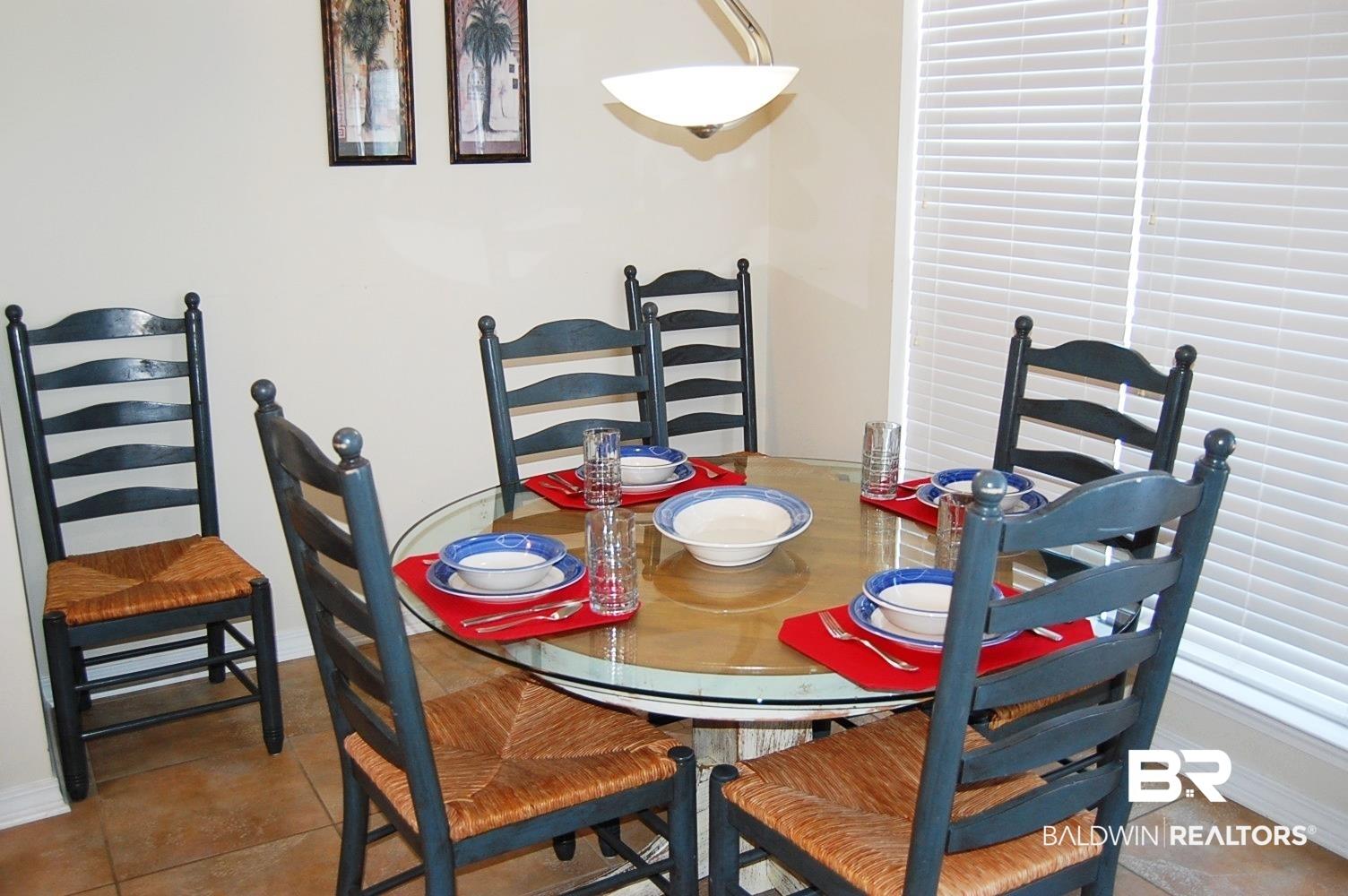 Image 4: Dining area featuring a circular glass-top table, tile flooring, and a window with horizontal blinds over looking the spacious balcony.