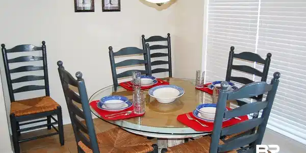 Image 4: Dining area featuring a circular glass-top table, tile flooring, and a window with horizontal blinds over looking the spacious balcony.