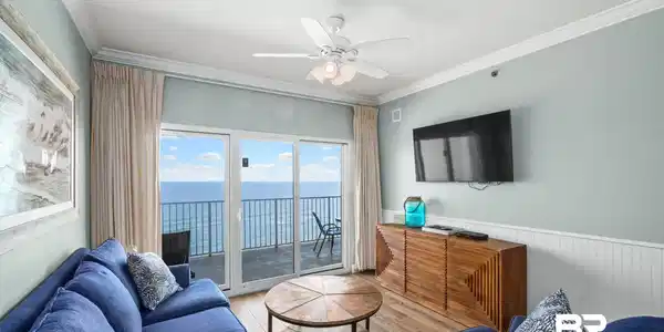 Image 4: Living area featuring a spacious balcony with ocean scenery, wood-finish flooring, white crown molding, and a ceiling fan with integrated lighting