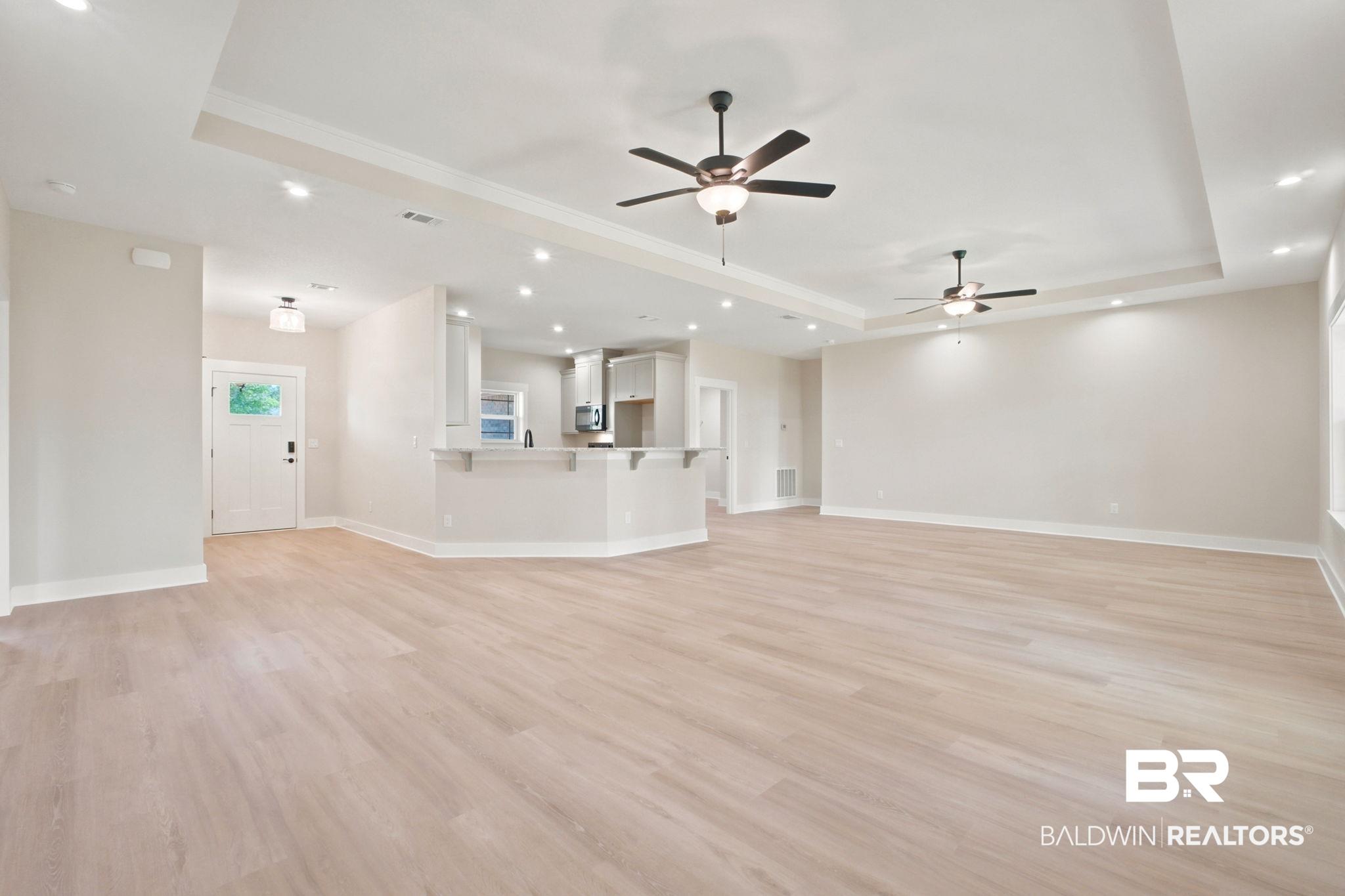 Image 3: Open-concept living space featuring wood-finish flooring, recessed lighting, ceiling fans, tray ceilings, and a breakfast bar