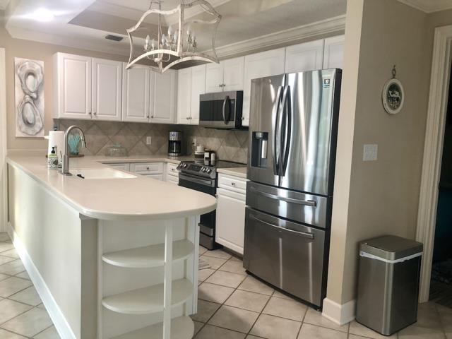 Image 2: Kitchen with stainless steel appliances, light countertops, open shelves, white cabinets, and a peninsula