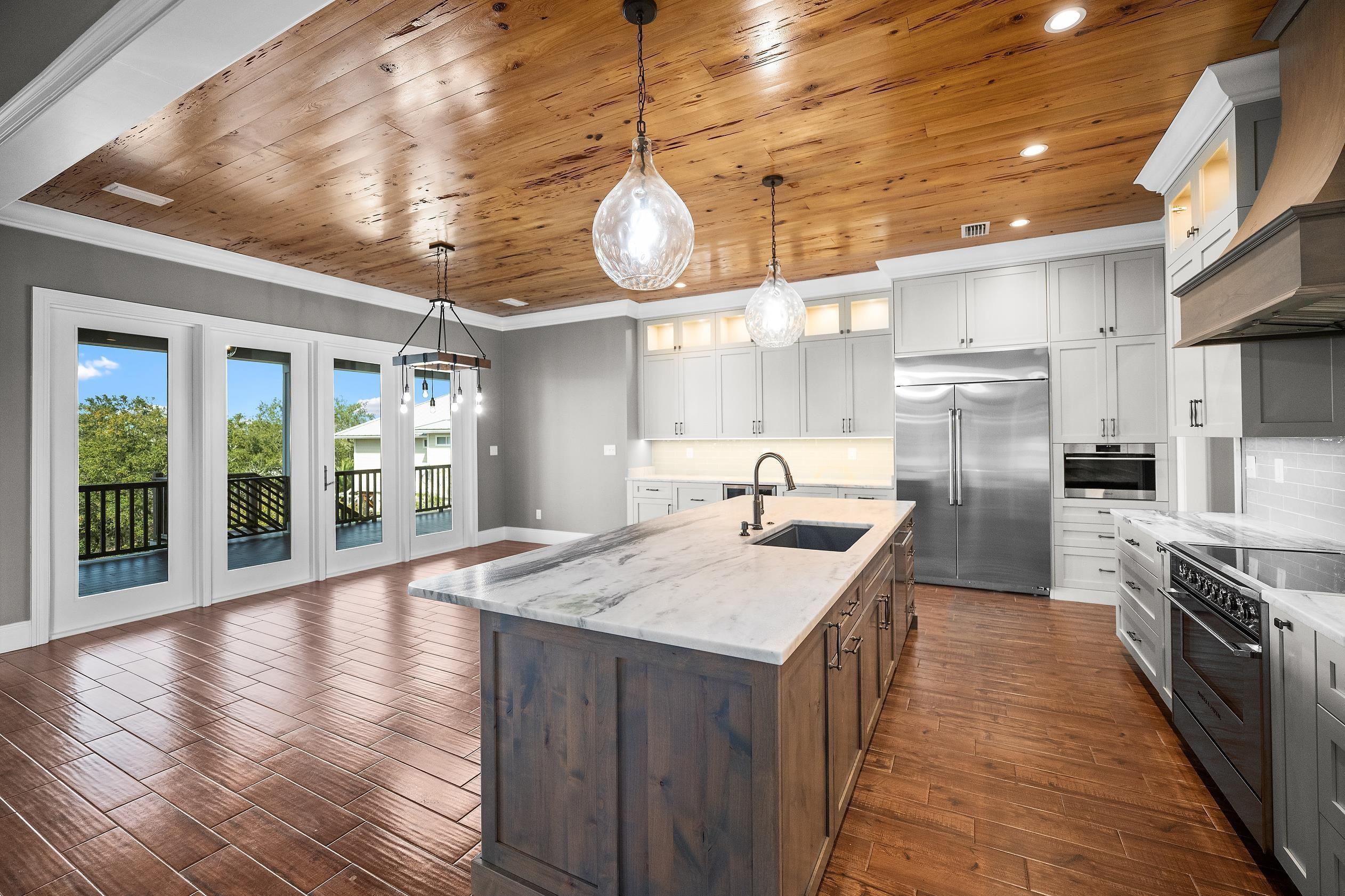 Image 4: Two tone kitchen featuring wood ceiling, dual tone cabinets, stainless steel appliances, light stone counters, and glass fronted cabinets