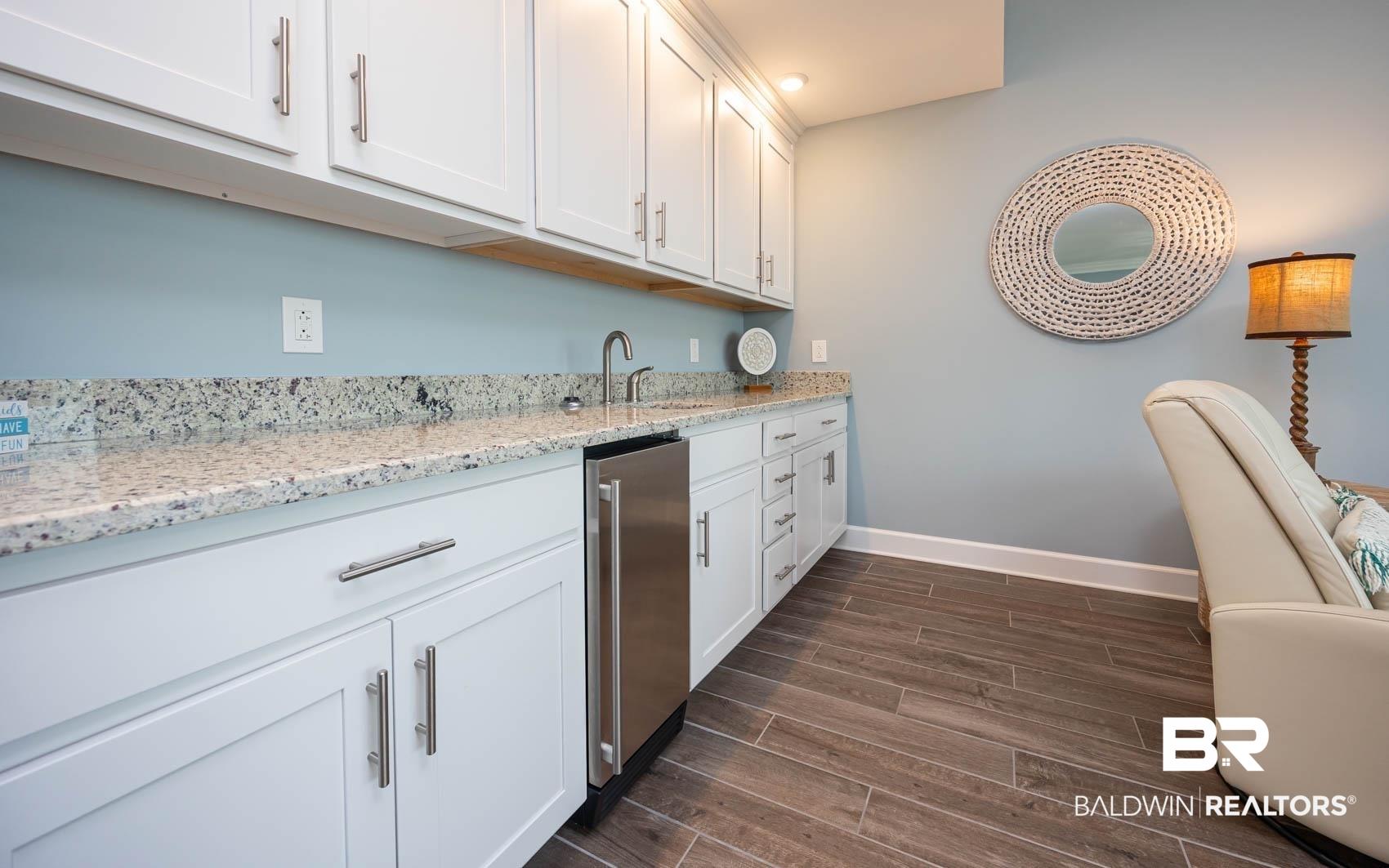 Image 4: Kitchen featuring white cabinetry, light stone counters, and wood tiled floors