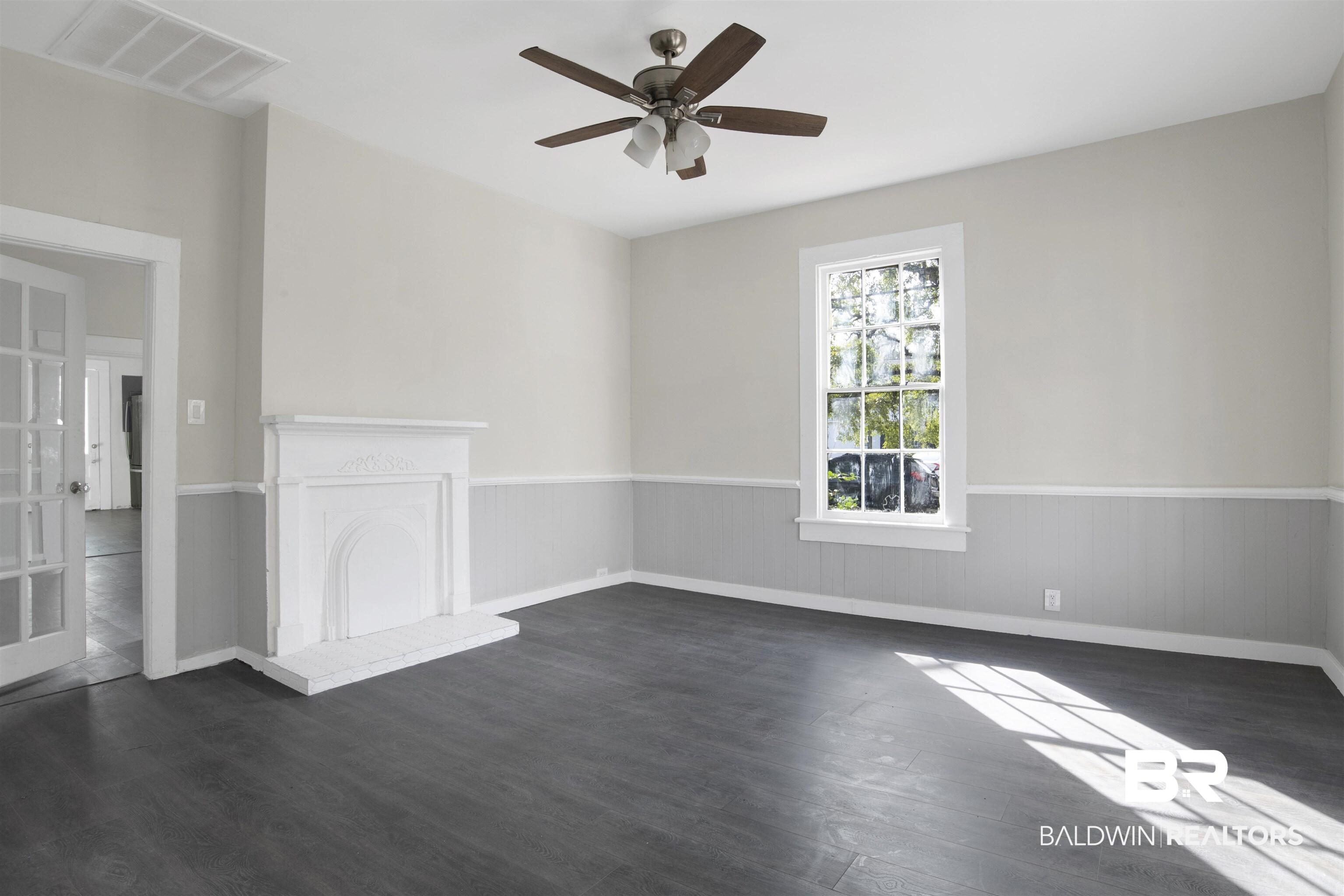 Image 4: Unfurnished room featuring ceiling fan, dark wood-style floors, wainscoting, and a fireplace with raised hearth