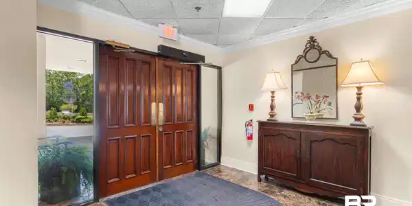 Image 4: Rich wood double doors with brass hardware, expansive glass sidelights, and polished marble-look flooring