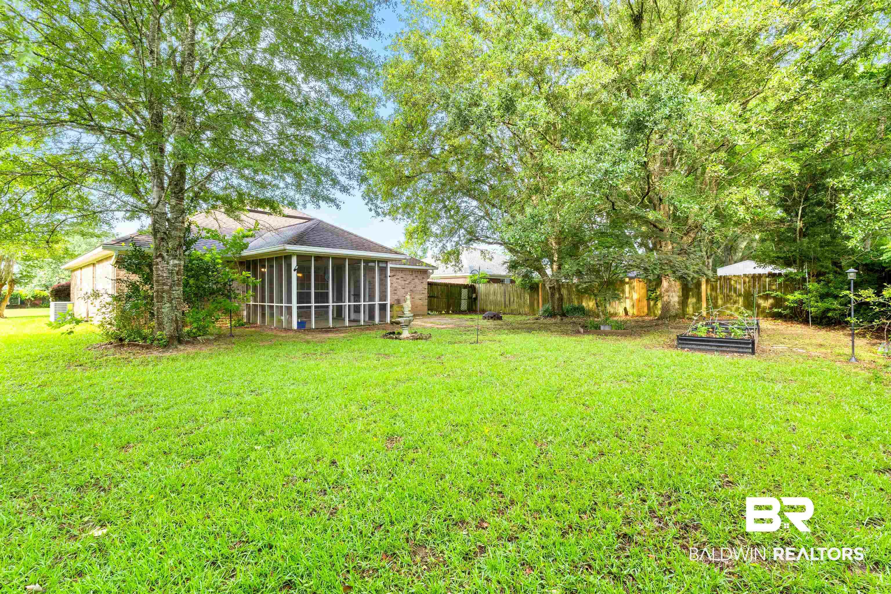 Image 2: Expansive backyard featuring a large screened-in porch, mature trees, a raised garden bed, and a wood privacy fence