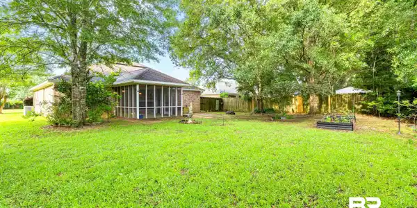 Image 2: Expansive backyard featuring a large screened-in porch, mature trees, a raised garden bed, and a wood privacy fence