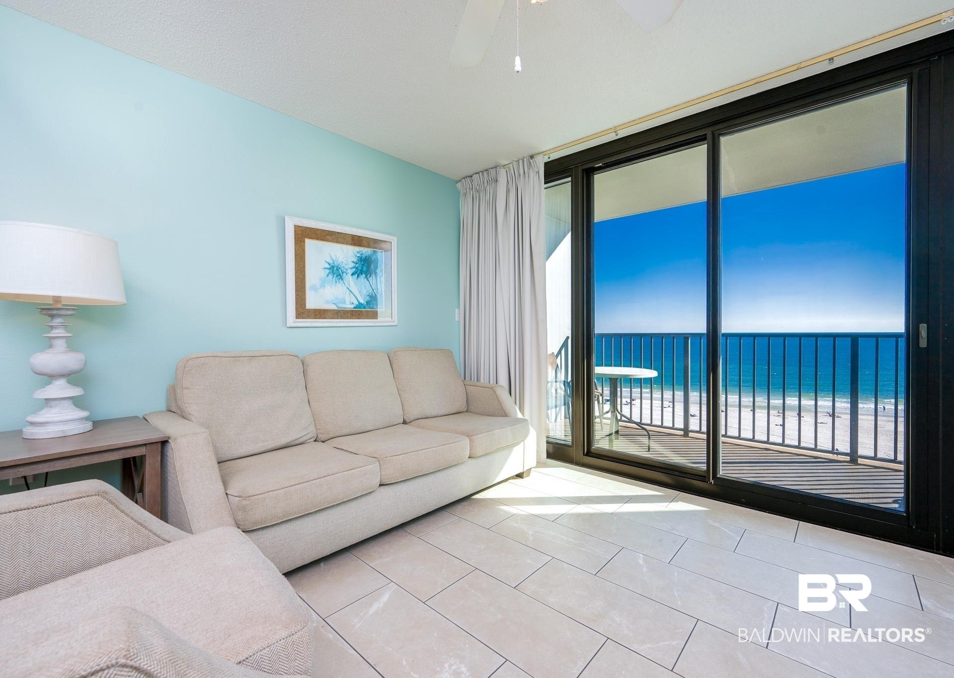 Image 3: Tiled living area featuring view of water and beach, expansive windows, and a ceiling fan