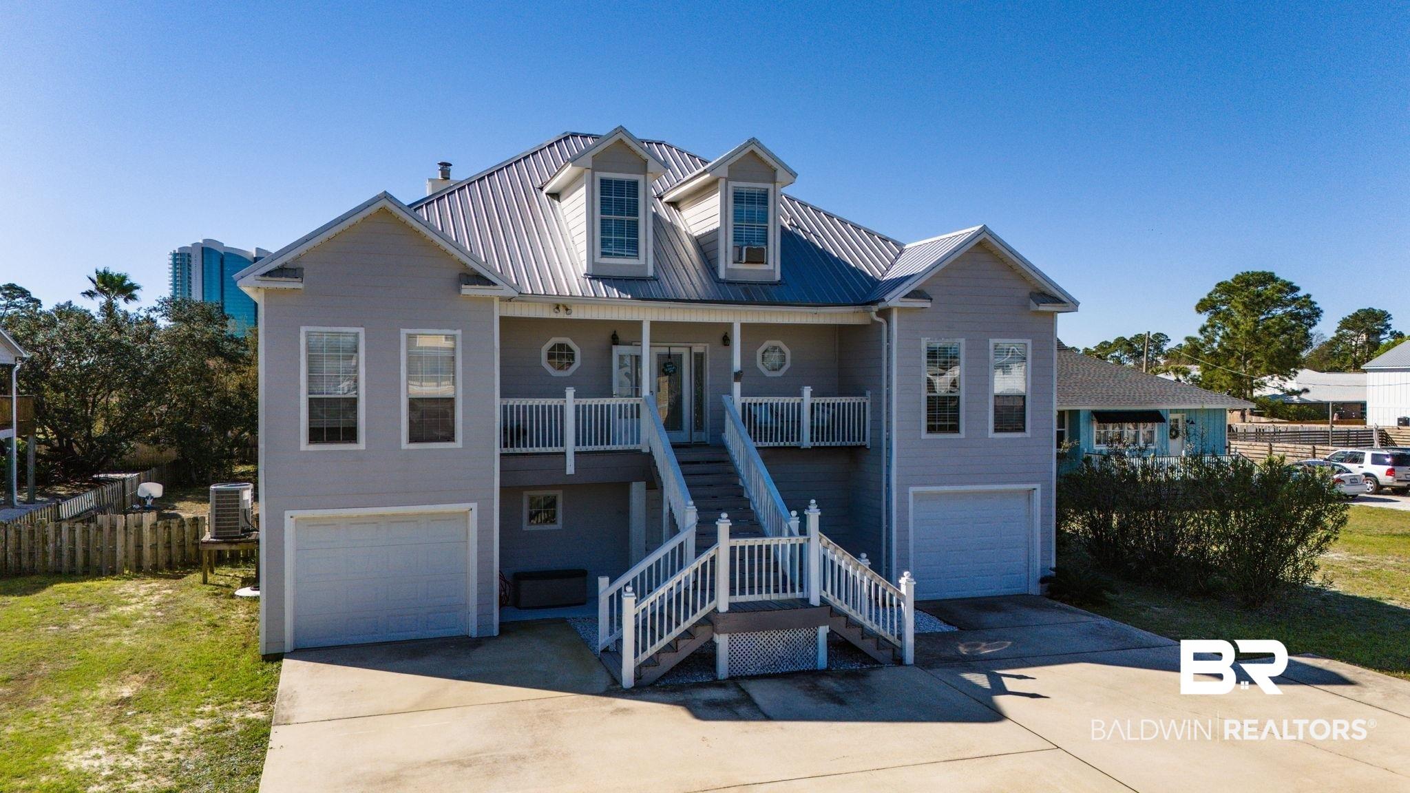 Image 4: Raised beach house featuring a garage, a metal roof, concrete driveway, and a porch
