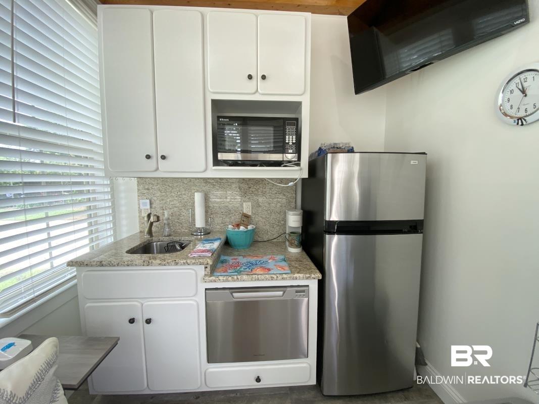 Image 3: Compact kitchen with white cabinetry, granite-finish countertops, stainless steel sink, and stainless steel appliances including a refrigerator, microwave, and dishwasher