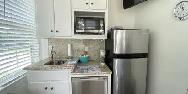 Image 3: Compact kitchen with white cabinetry, granite-finish countertops, stainless steel sink, and stainless steel appliances including a refrigerator, microwave, and dishwasher