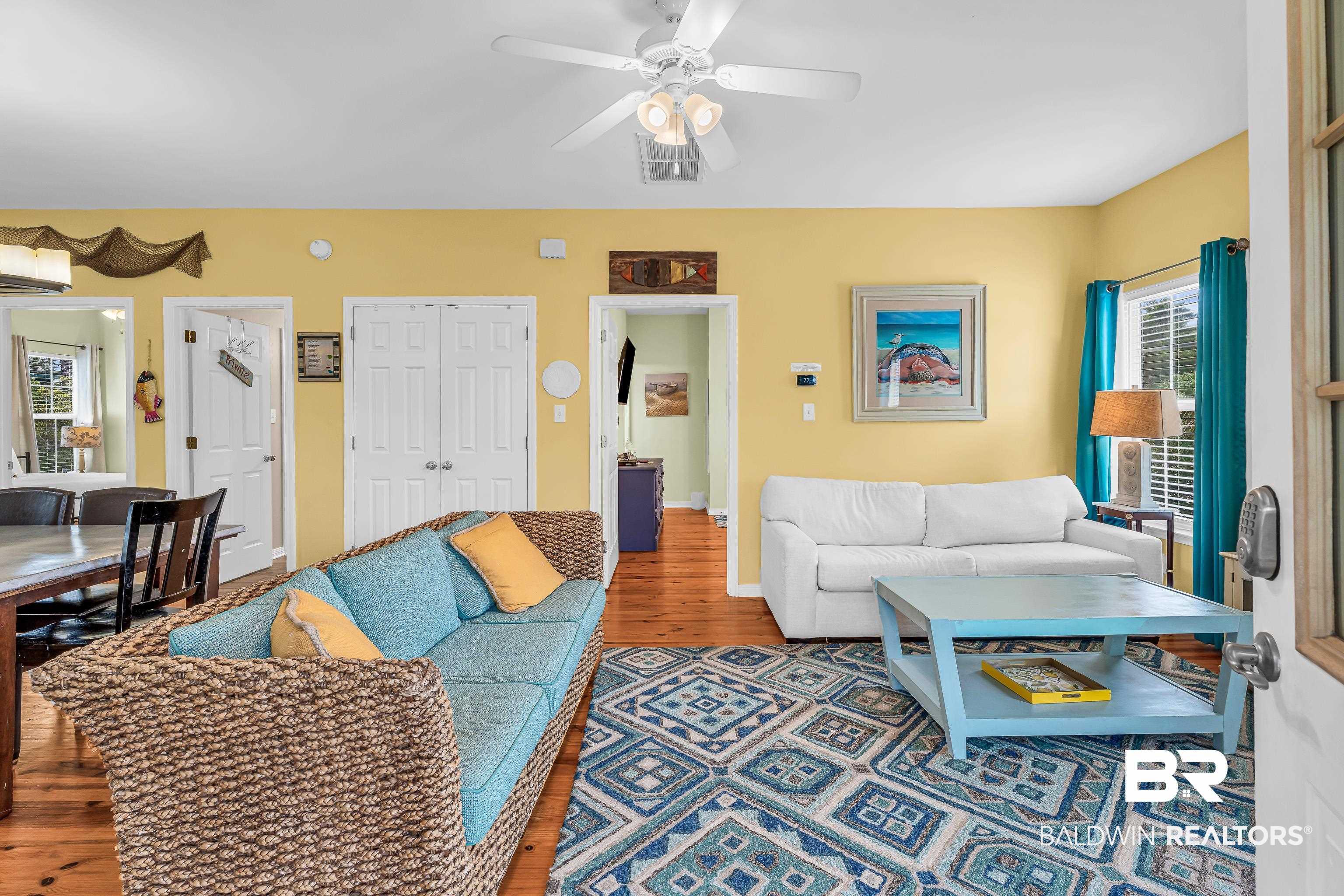 Image 3: Living area featuring warm yellow walls, wood-finish flooring, and a white ceiling fan