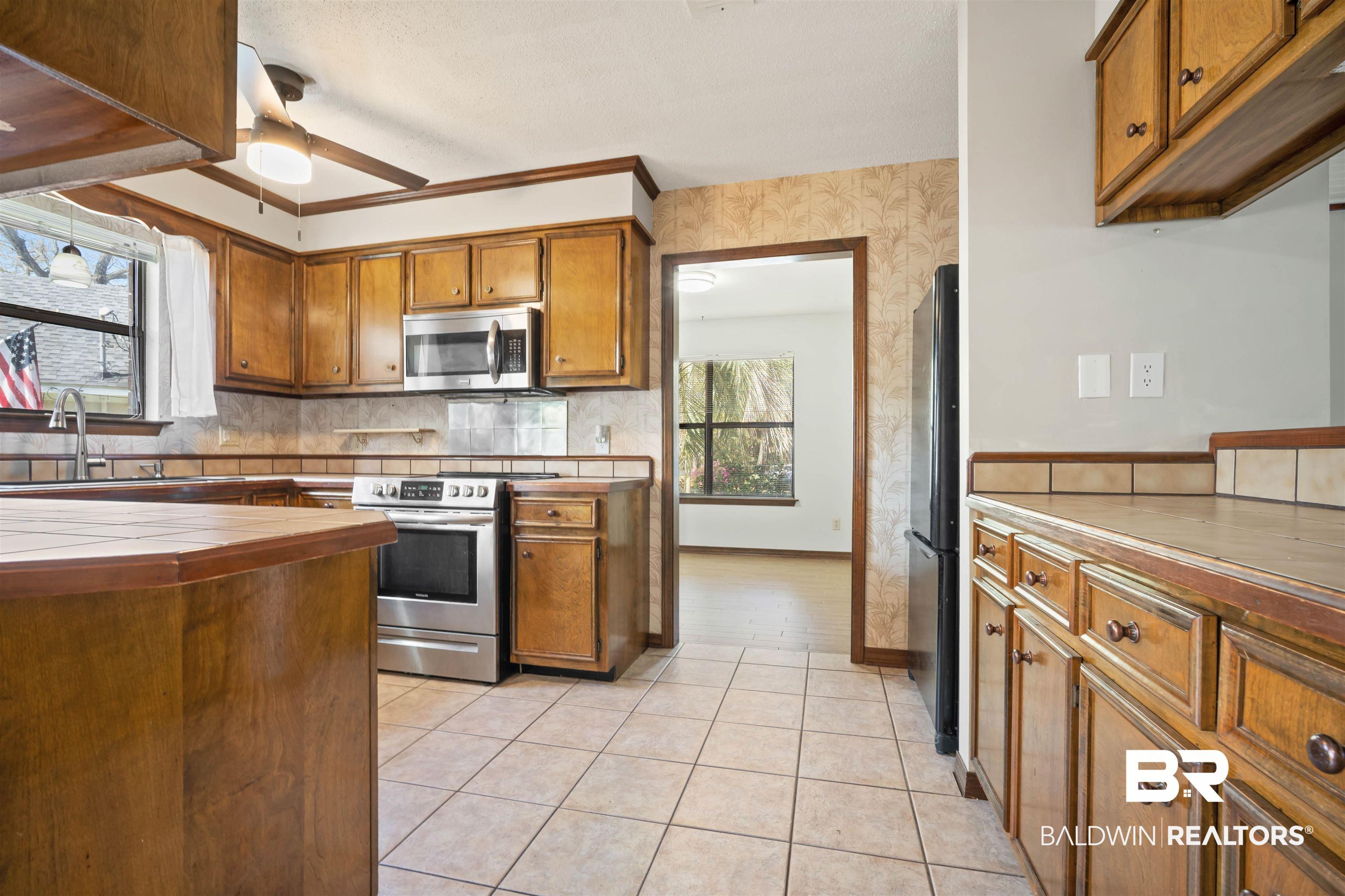 Image 3: Kitchen featuring wood finish cabinets, stainless steel appliances, tile counters, tasteful backsplash, and wallpapered walls