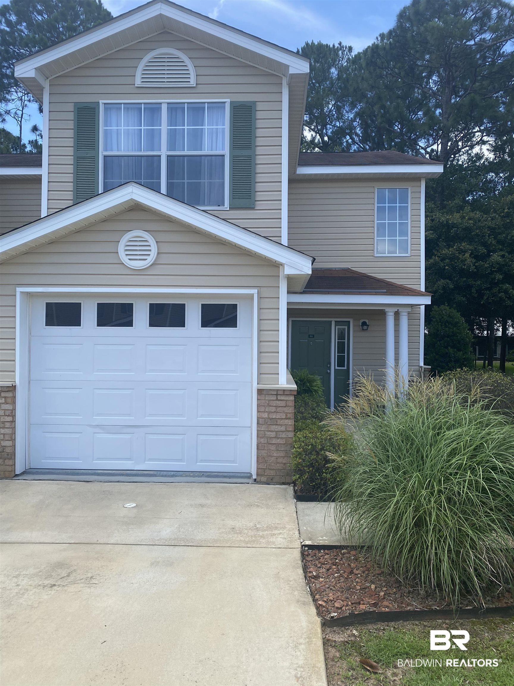 Image 1: Two-story property featuring light-colored siding, a prominent white garage door with upper window panels, and a covered entry with a green front door