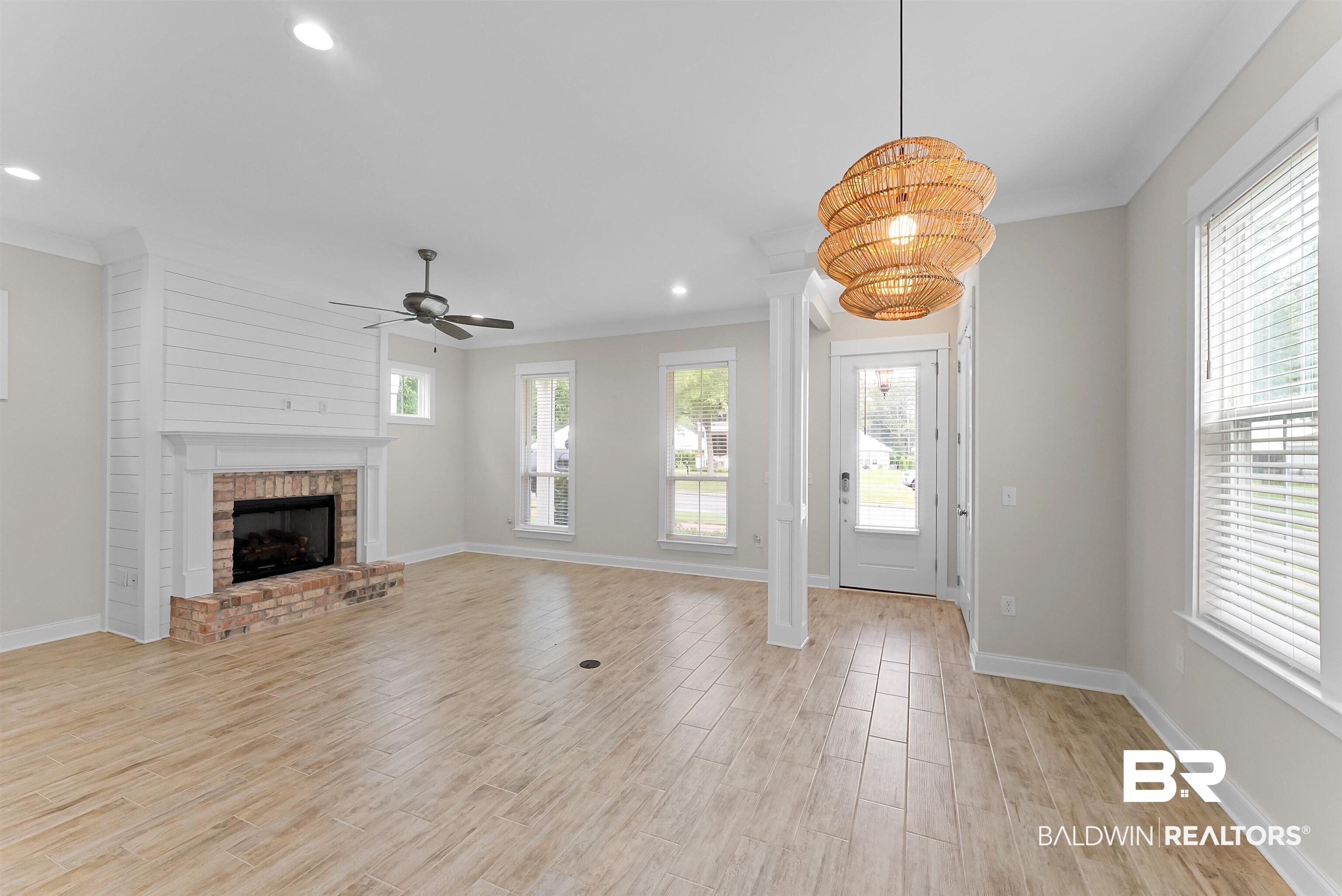 Image 2: Spacious living area featuring light wood-finish flooring, a brick fireplace with a shiplap accent wall, and a ceiling fan