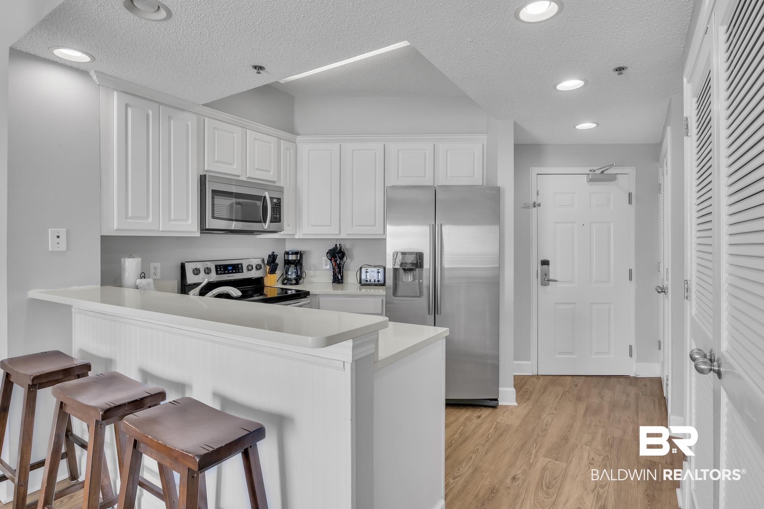 Image 2: Kitchen with a textured ceiling, a breakfast bar area, stainless steel appliances, light wood finished floors, and a peninsula