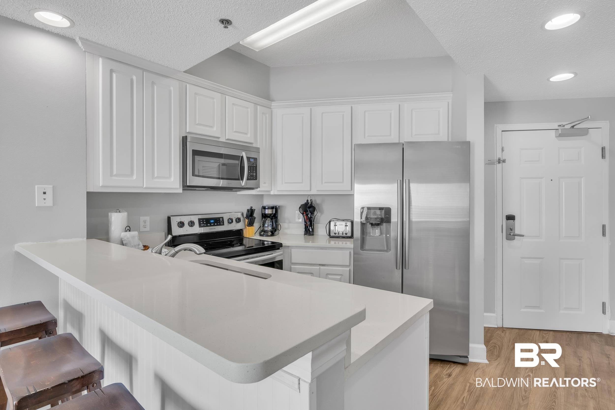 Image 3: Kitchen with a kitchen breakfast bar, a peninsula, light wood-style flooring, appliances with stainless steel finishes, and white cabinetry