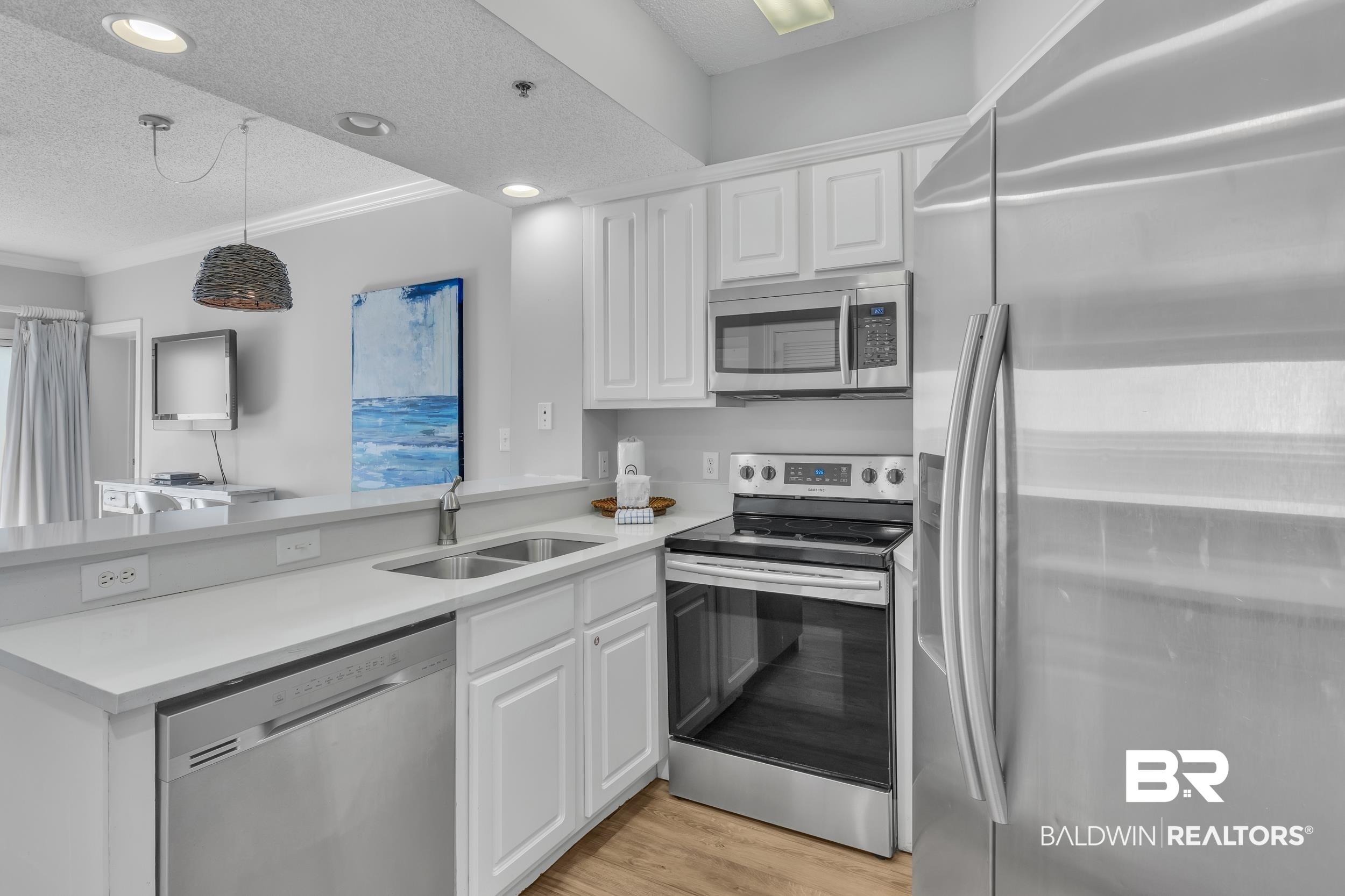 Image 4: Kitchen featuring a sink, a peninsula, a textured ceiling, appliances with stainless steel finishes, and white cabinetry