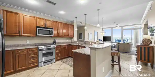 Image 2: Open-concept kitchen featuring wood cabinetry, stainless steel appliances, granite countertops, and tile flooring
