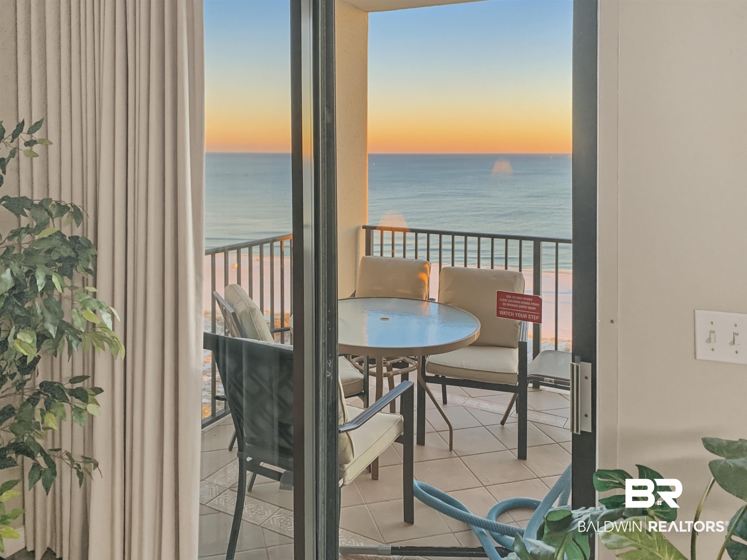 Image 4: Balcony at dusk with view of water and beach and outdoor dining space