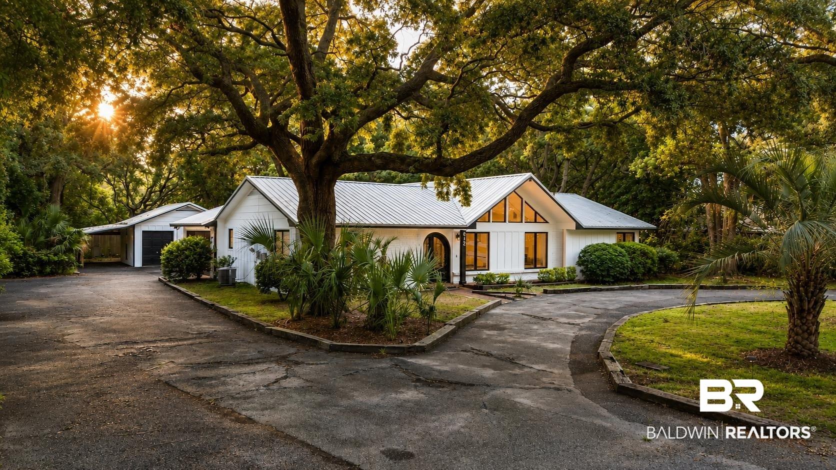Image 1: White exterior with a prominent metal roof and a large, mature tree providing natural shade