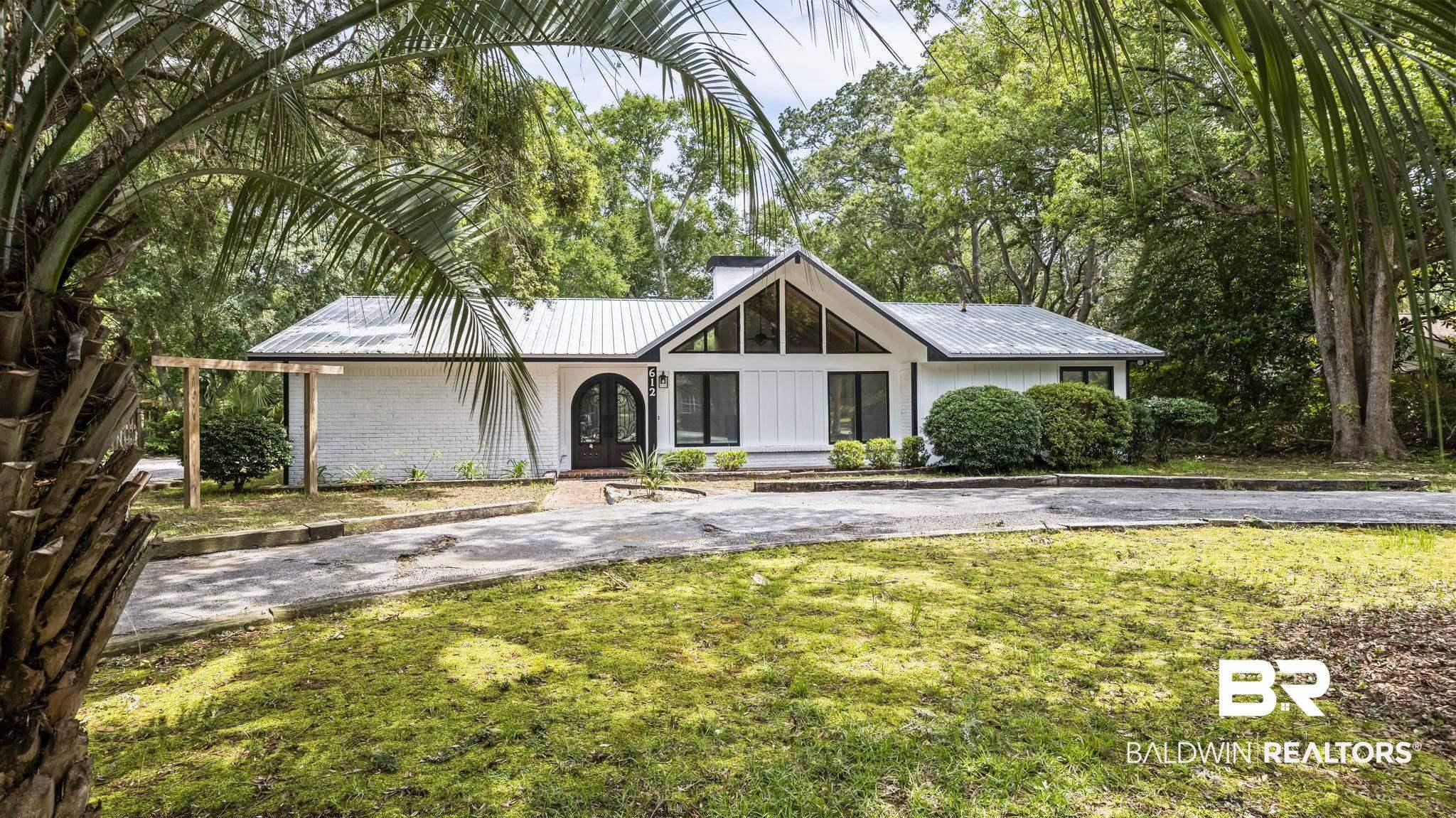 Image 3: Contemporary white exterior featuring a gabled roofline with large windows, an arched entry door, a metal roof, and a mature tree canopy surround