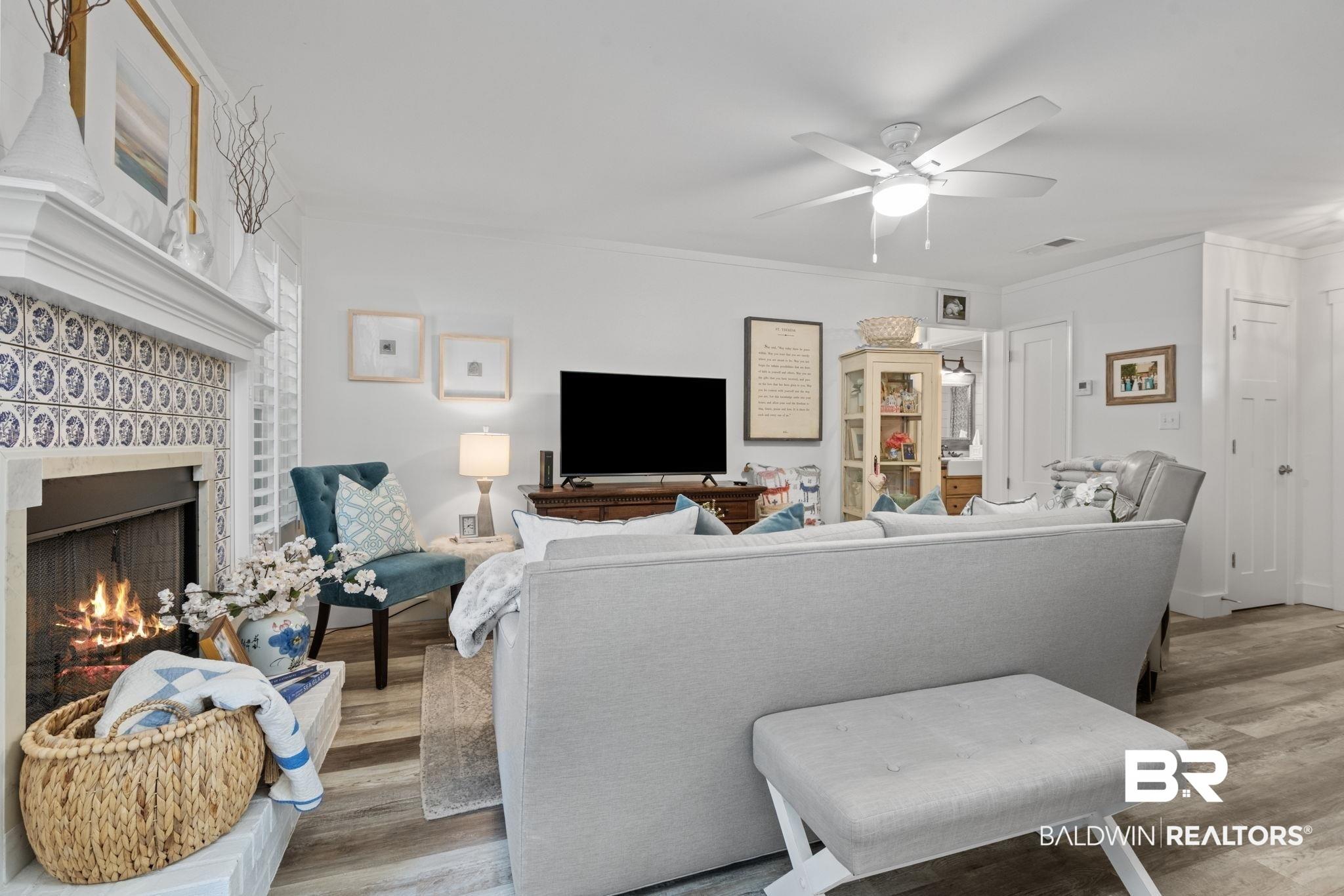 Image 4: Living room with ornamental molding, wood finished floors, a warm lit fireplace, and ceiling fan
