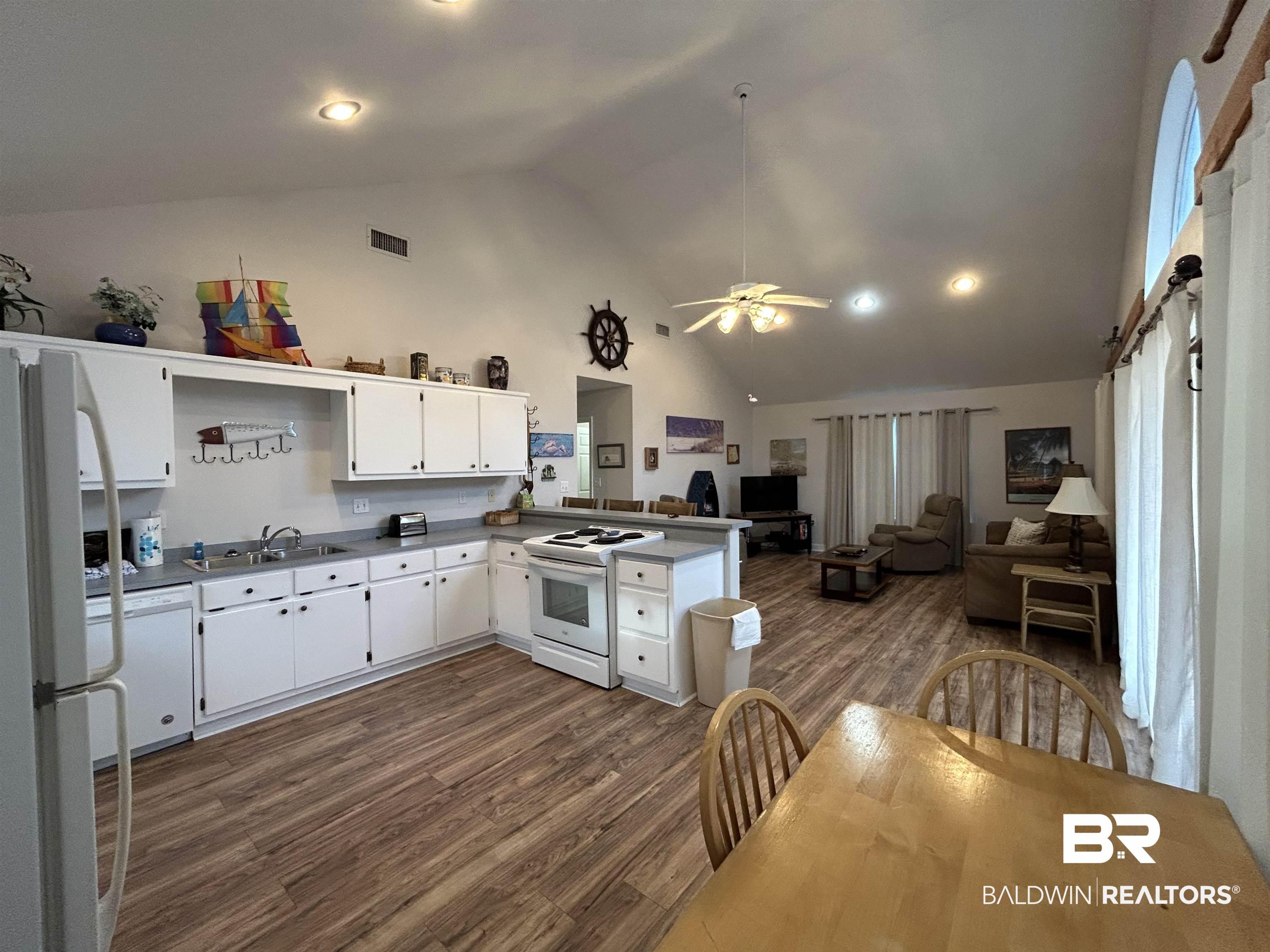 Image 2: Kitchen and living space featuring vaulted ceilings, wood-finish flooring, white cabinetry, integrated appliances, and recessed lighting