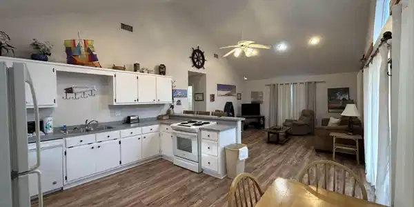 Image 2: Kitchen and living space featuring vaulted ceilings, wood-finish flooring, white cabinetry, integrated appliances, and recessed lighting
