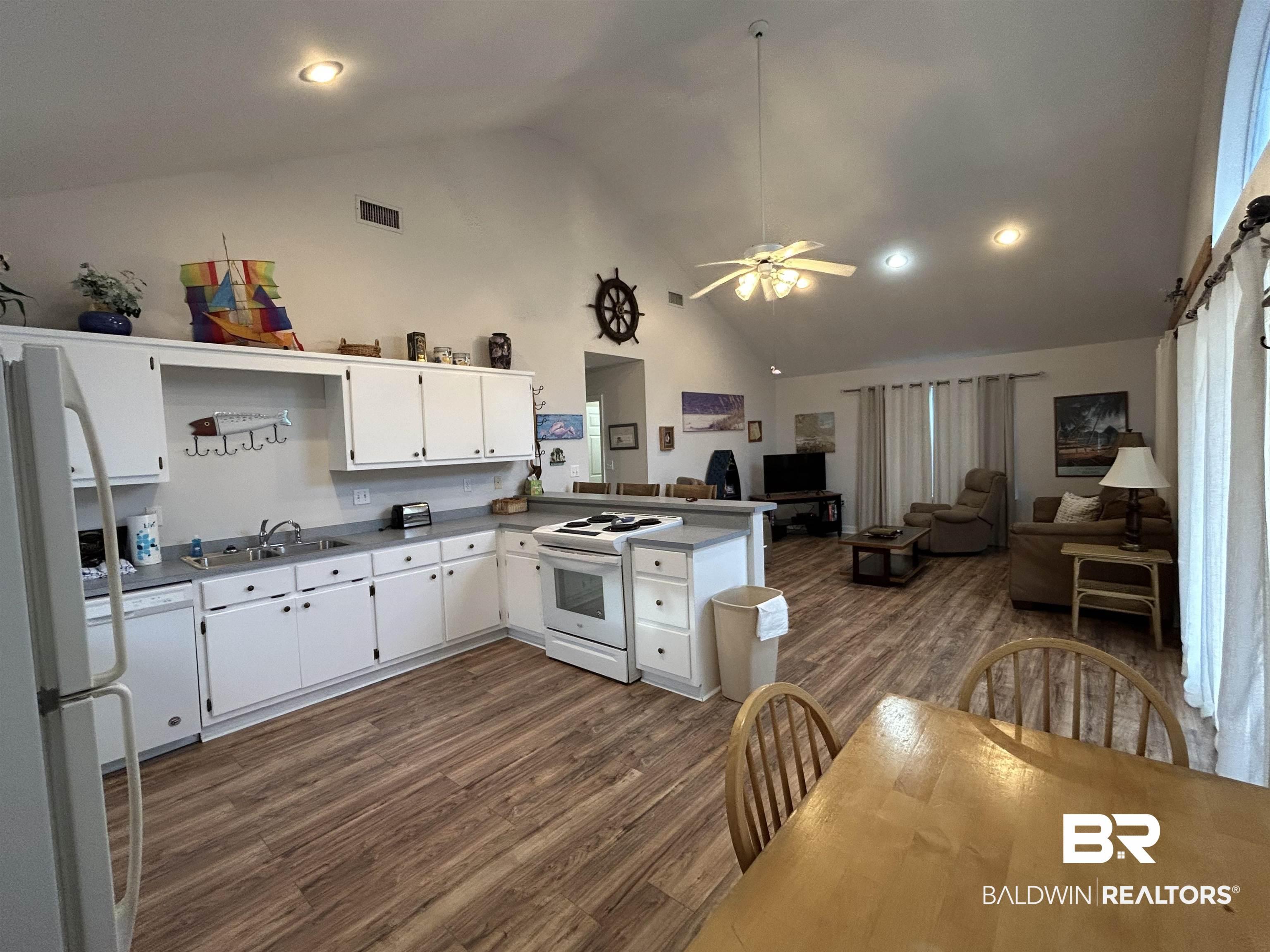 Image 3: Open-concept interior featuring wood-finish flooring, vaulted ceilings with recessed lighting, and a kitchen with white cabinetry and light countertops