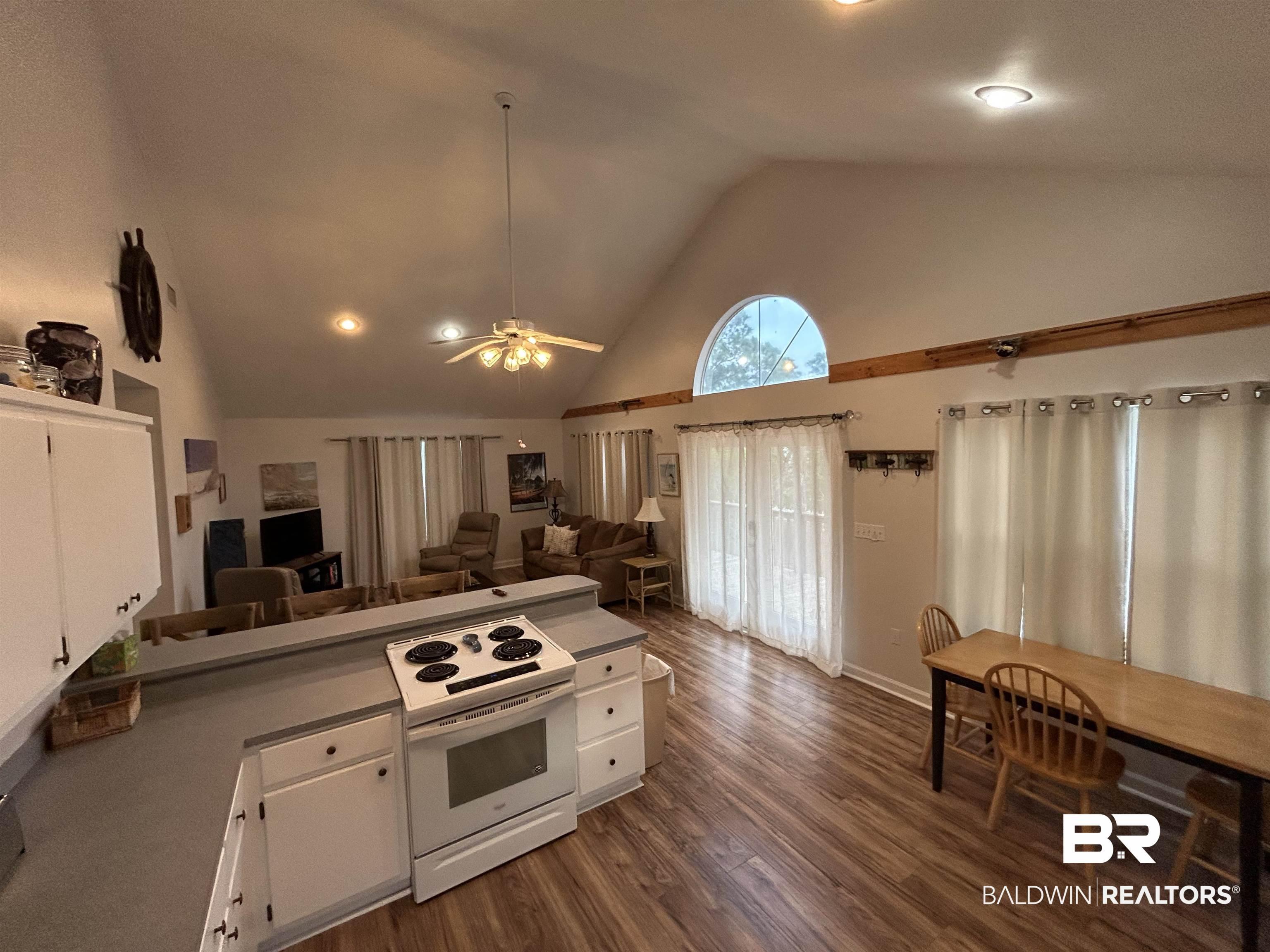 Image 4: Open-concept living space featuring vaulted ceilings, wood-finish flooring, a kitchen island with built-in range, and a large arched window