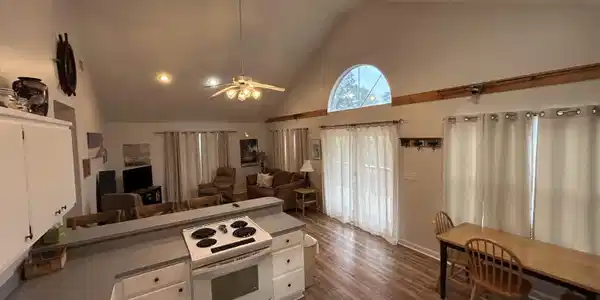 Image 4: Open-concept living space featuring vaulted ceilings, wood-finish flooring, a kitchen island with built-in range, and a large arched window